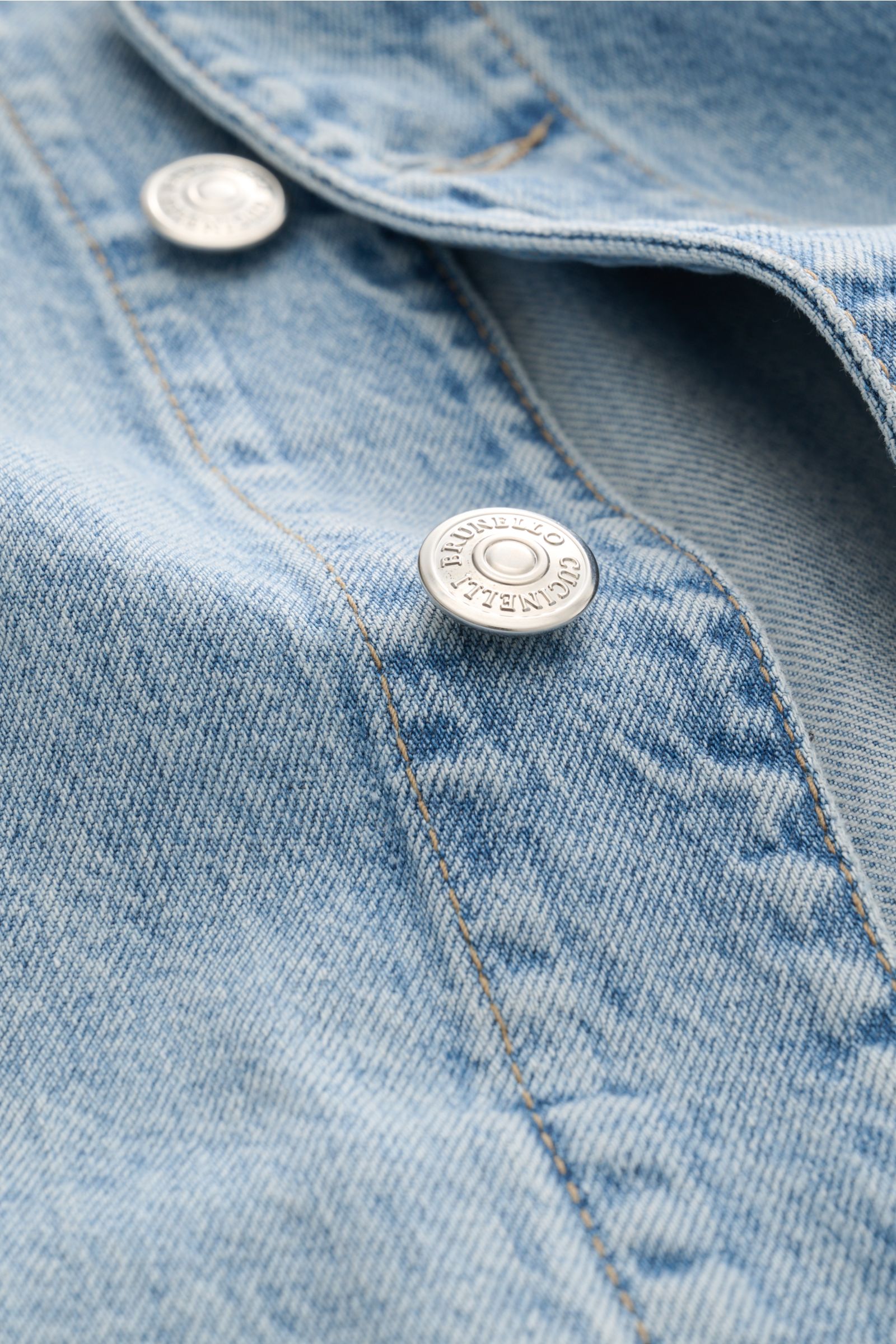 Brunello Cucinelli Jeansjacke rauchblau close-up from above showing silver logo buttons and detailed cotton denim fabric texture.  
Edles Casual-Piece: Die Jeansjacke von BRUNELLO CUCINELLI aus reiner Baumwolle ergänzt anspruchsvolle Freizeitgarderoben