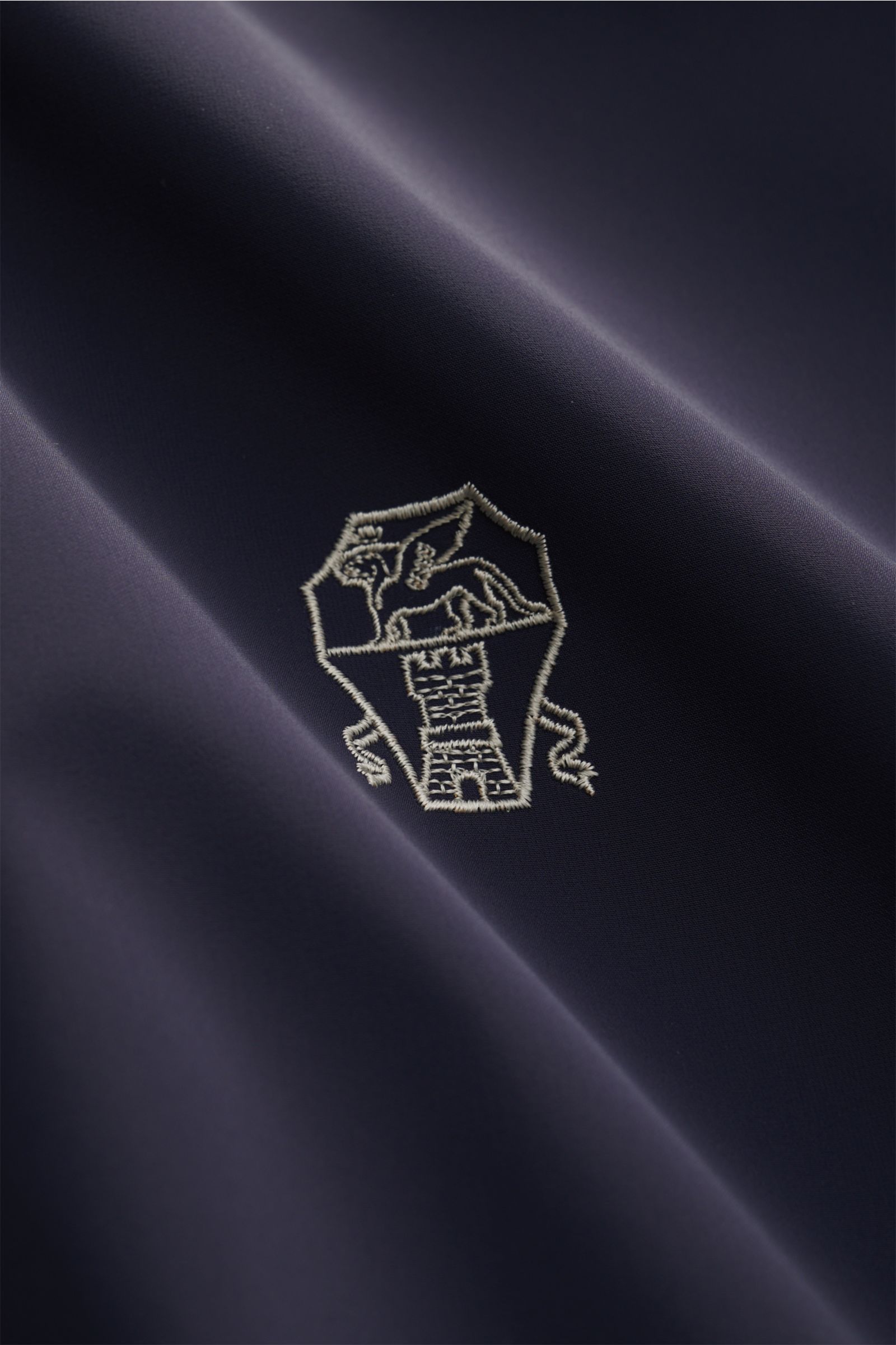 Close-up front view of the navy fabric with embroidered Solomeo logo on the Brunello Cucinelli Wendeblouson navy/grau, a reversible, wind- and water-repellent blouson made of high-quality microfiber and cashmere-silk jersey, featuring a smooth touch, brea