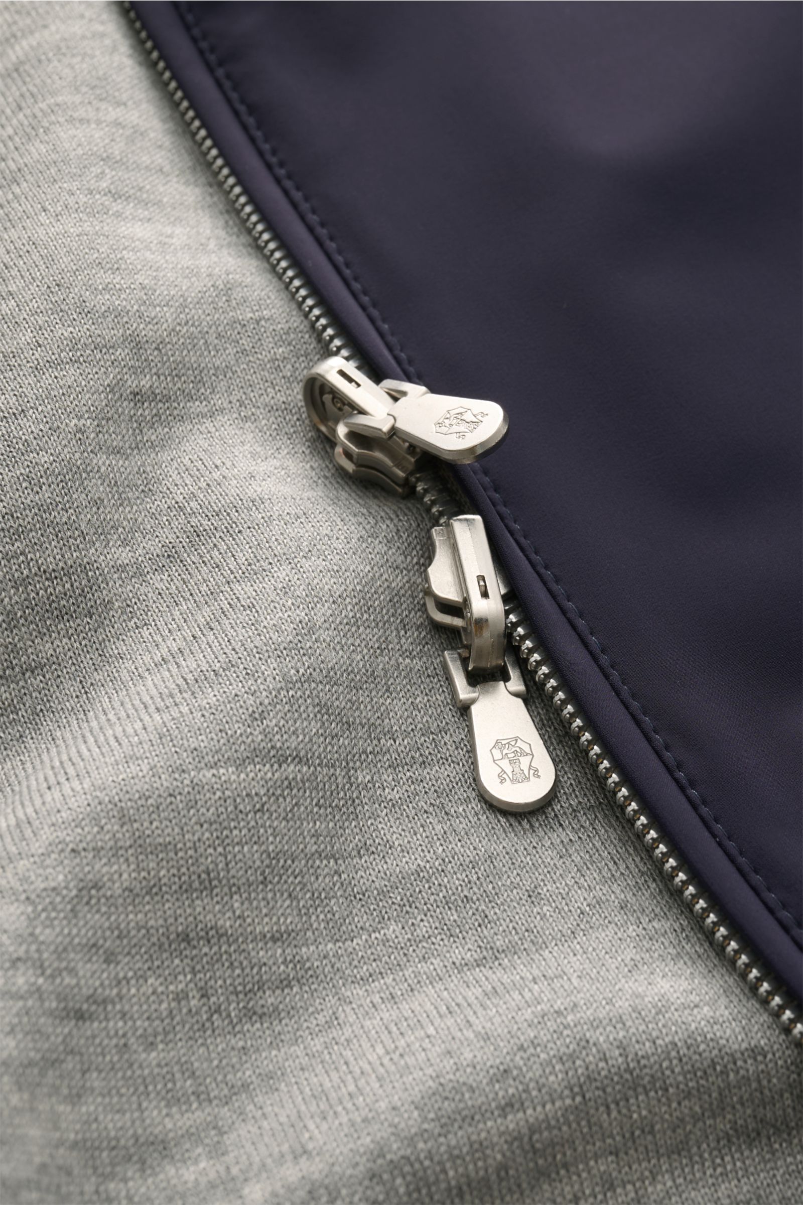 Close-up front view of the Brunello Cucinelli Wendeblouson navy/grau showing the silver dual zipper detail and fabric texture, highlighting the wind- and water-repellent microfiber navy side and soft grey cashmere-silk jersey inner side. Zwei Looks, ei
