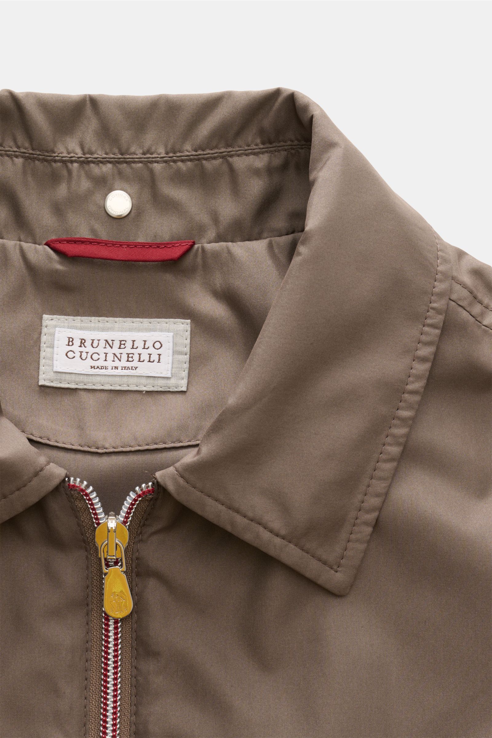 Close-up front view of the taupe Brunello Cucinelli Jacke collar, zipper, and label, showcasing its smooth silk and microfiber mix, slim fit, and unconstructed design. Luxuriöse Leichtigkeit: Die Jacke von BRUNELLO CUCINELLI überzeugt mit einem erlesenen 