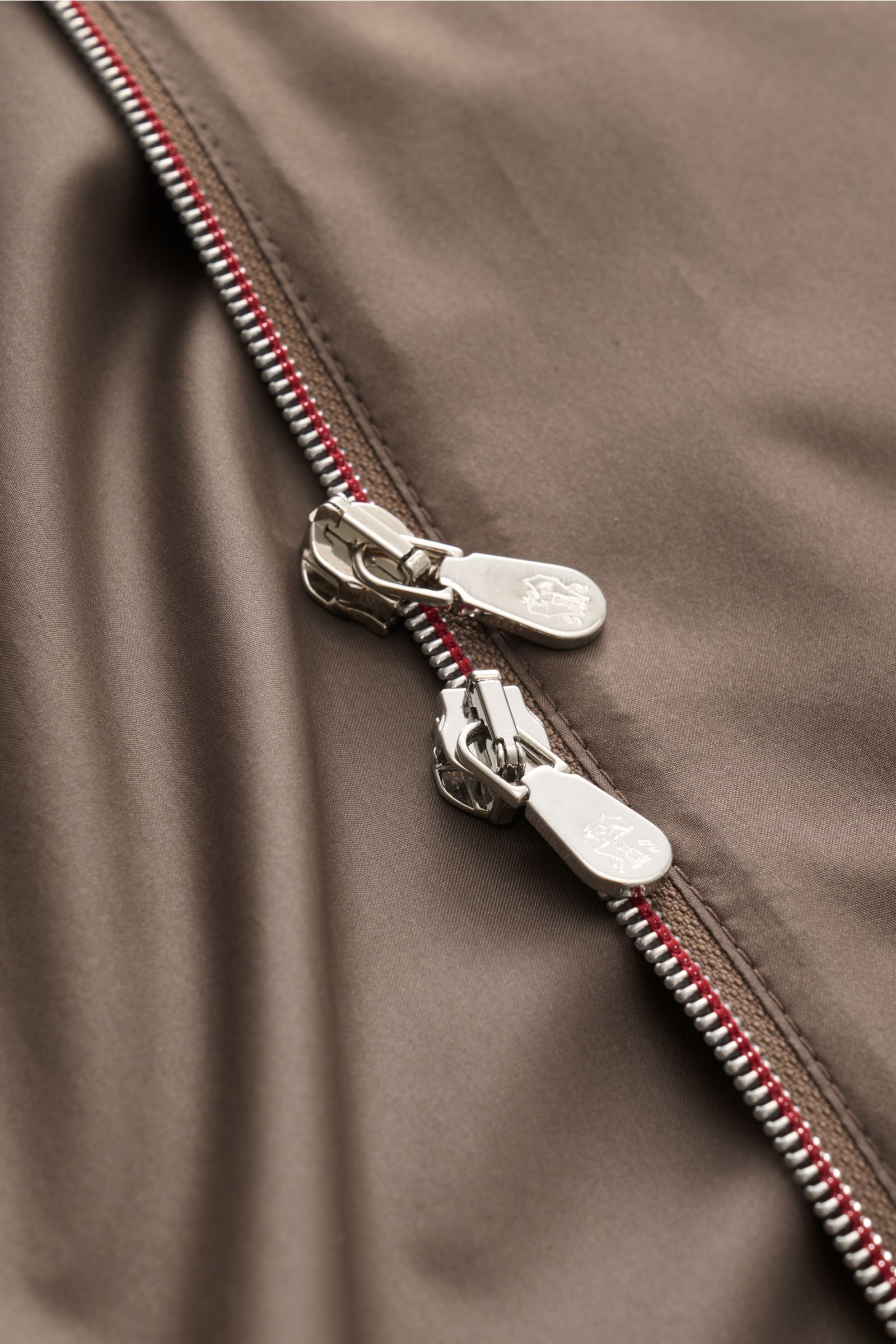 Close-up top-down view of the taupe Brunello Cucinelli Jacke showing its silver two-way zipper on smooth silk and microfiber blend fabric with a slim fit and unconstructed design. Luxuriöse Leichtigkeit: Die Jacke von BRUNELLO CUCINELLI überzeugt mit eine