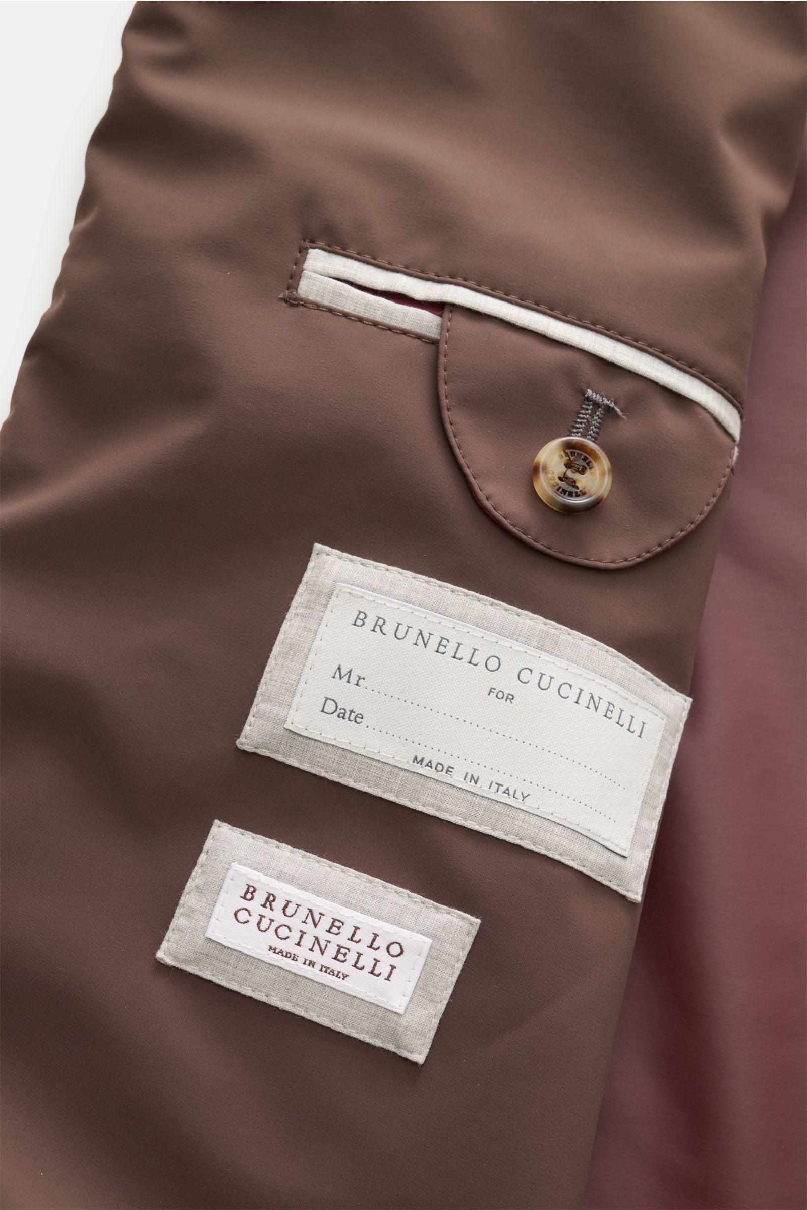 Close-up image of the inside of the Brunello Cucinelli Blouson grau meliert, showing a brown fabric pocket with a button and two stitched labels. Leicht, edel und mit unverwechselbarer Präsenz: Dieser Blouson aus dem Hause BRUNELLO CUCINELLI erhält durch 