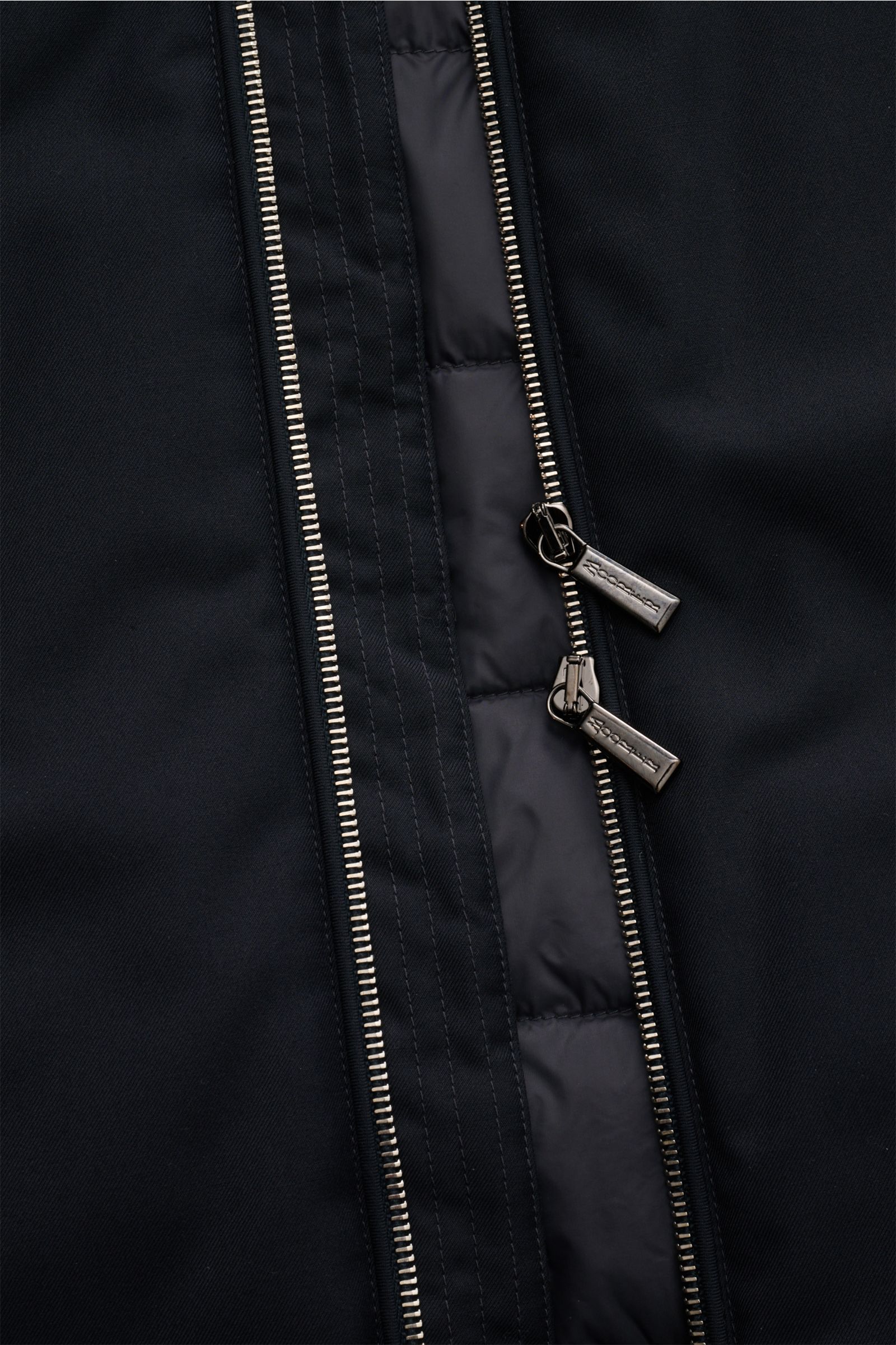 Nahaufnahme der zwei-Wege-Reißverschluss-Front der Moorer Daunenweste 'Uros' dark navy, gefertigt aus weichem, wind- und wasserabweisendem Garbadine-Gewebe.