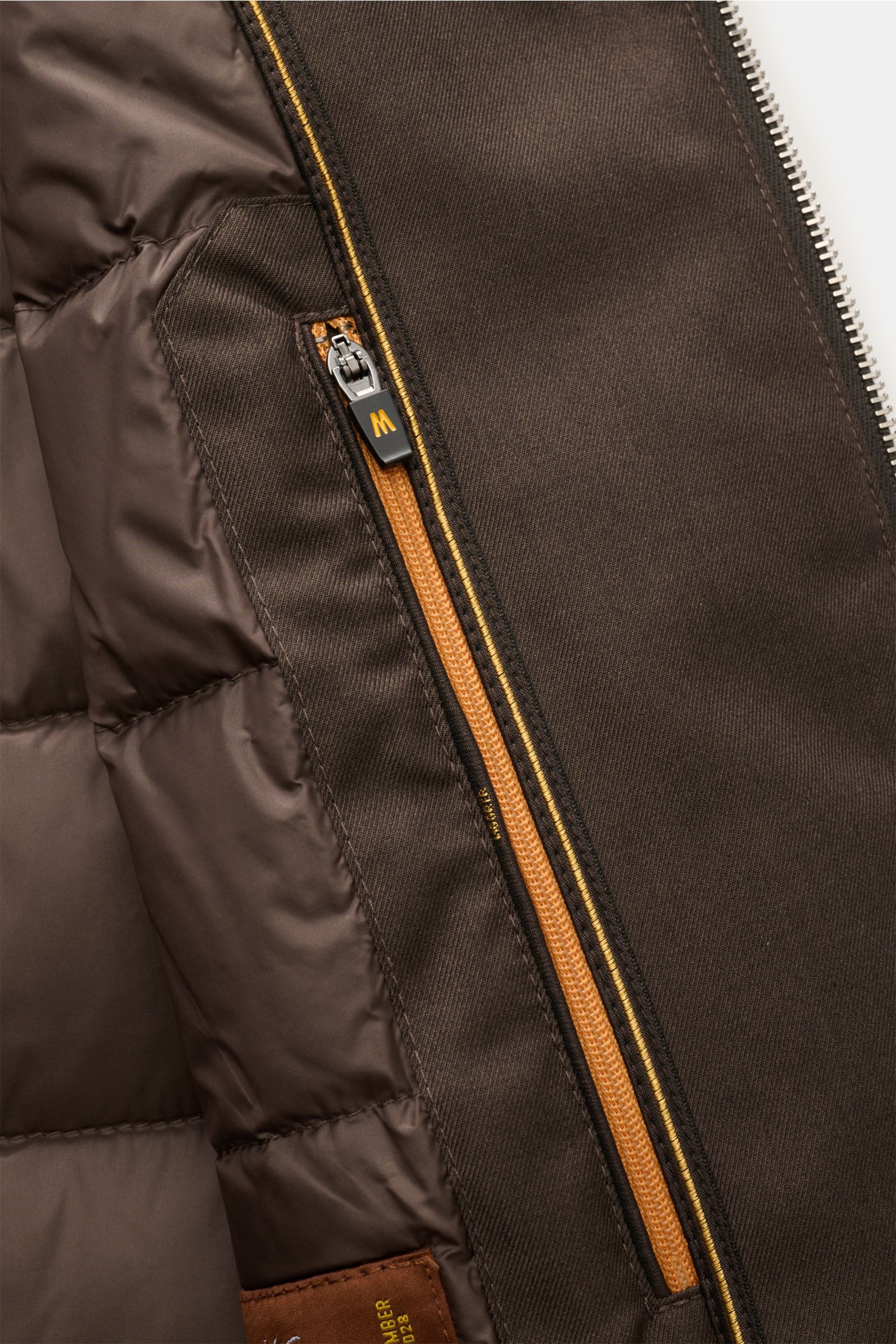 Nahaufnahme der Innenansicht der graubraunen Moorer Daunenweste 'Uros' mit wasserabweisendem Garbadine-Gewebe und zwei Innentaschen.