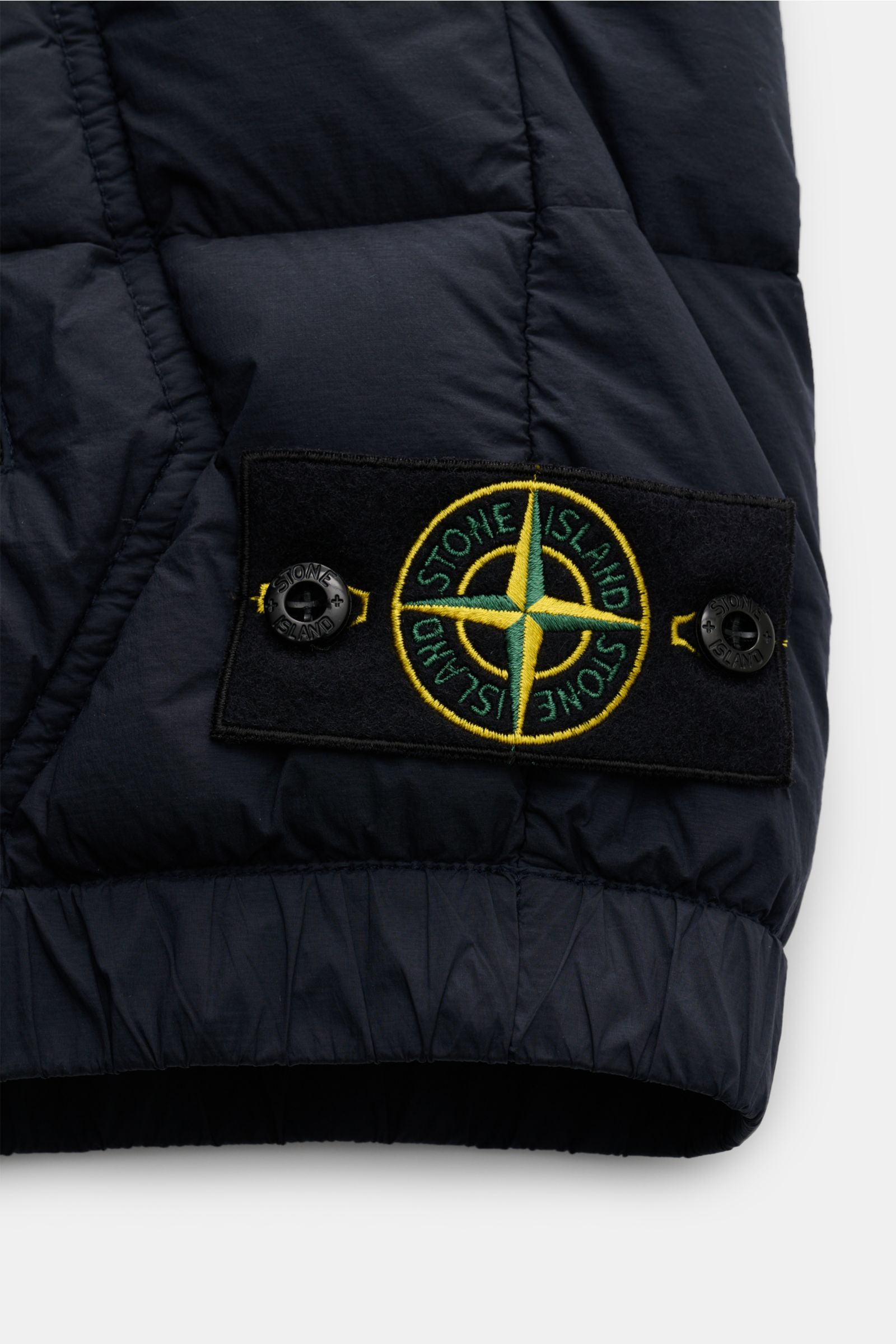 Stone Island Daunenweste 'Seamless Tunnel Nylon Down-TC' navy, Detailansicht des elastischen Saums und Kompass-Badge, hochwertige Microfaser, wärmende Daunenfüllung.