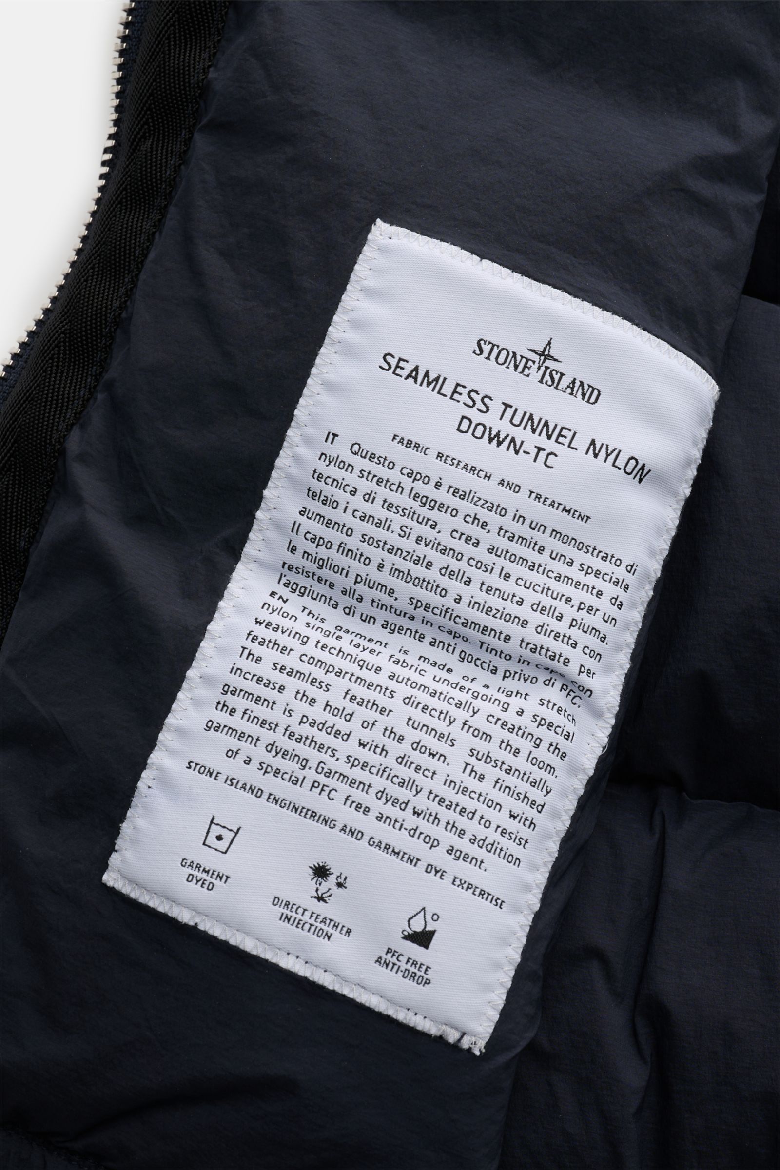 Nahaufnahme des weißen Labels innen der Stone Island Daunenweste 'Seamless Tunnel Nylon Down-TC' navy, hochwertige Microfaser, wärmende Daunenfüllung, Regular Fit, Reißverschluss, Stehkragen, Hüfttaschen, elastischer Saum.