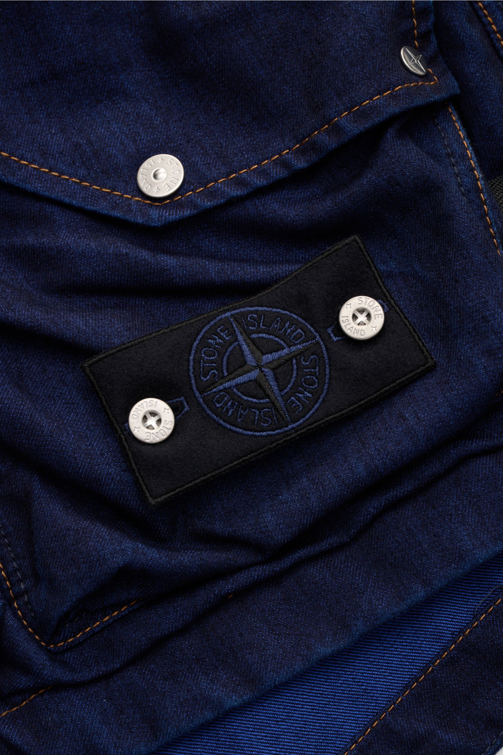 Stone Island Jeansweste 'Indigo Polypropylene Denim Light' dunkelblau, Detailaufnahme des Kompass-Badges und Naht aus schräger Perspektive, Baumwoll-Microfaser-Mix, Slim Fit, Utility-Look.