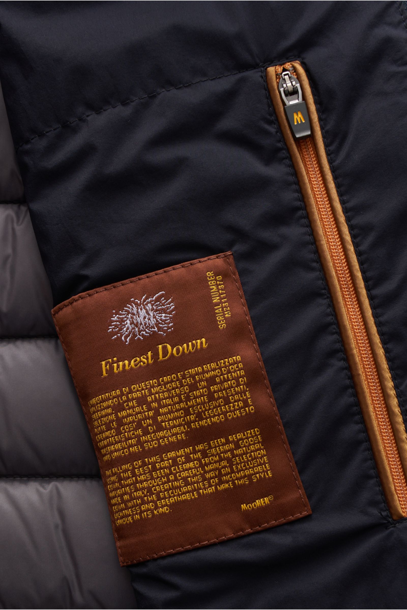 Nahaufnahme der Innenansicht der Moorer Daunenweste 'Calaf' navy mit braunem Etikett „Finest Down“ und orangem Zwei-Wege-Reißverschluss, atmungsaktive Microfaser, Gänsedaunenfüllung, schmaler Stehkragen, Slim Fit.