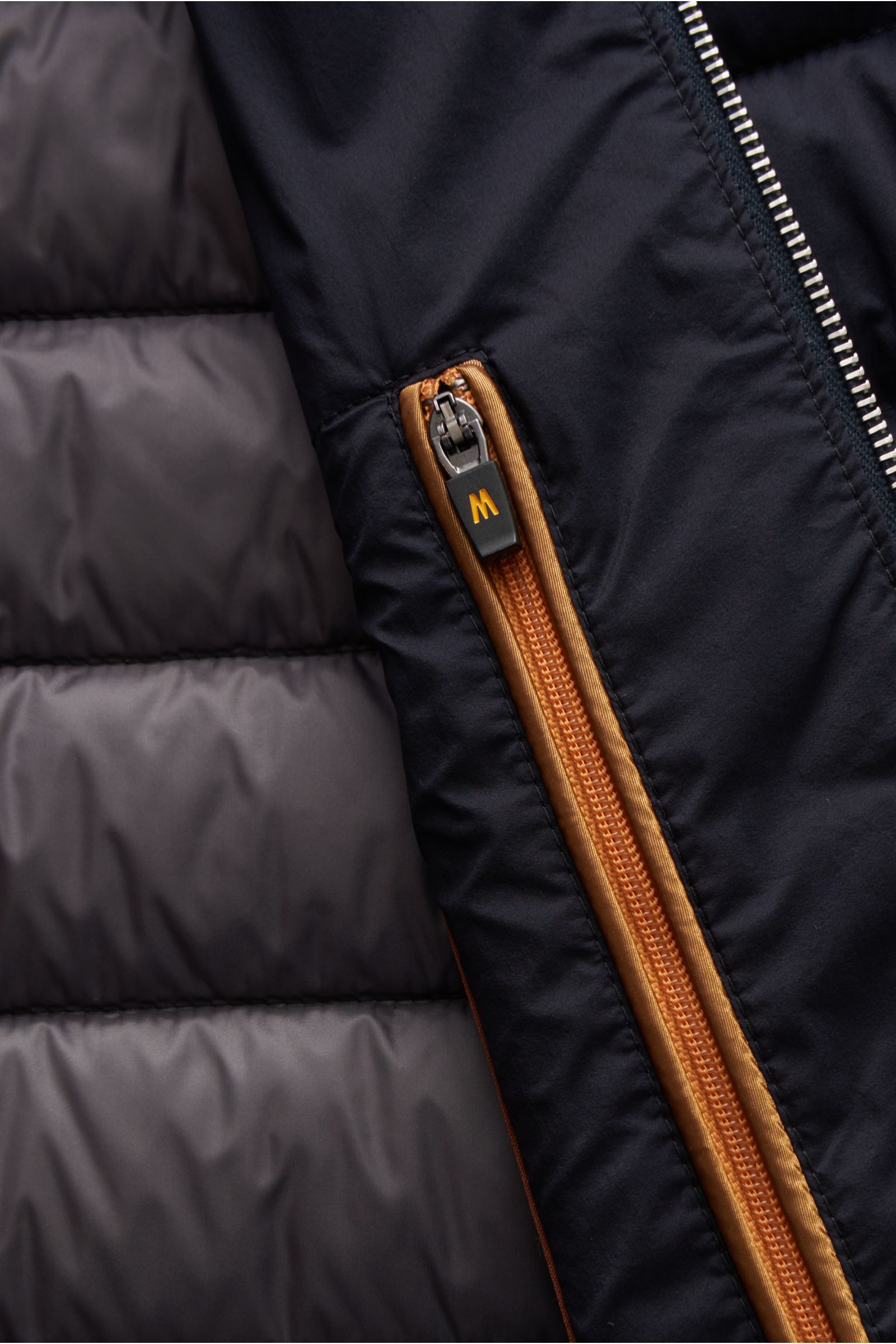 Nahaufnahme der schmal gesteppten Moorer Daunenweste 'Calaf' navy mit hochwertigem Microfaserstoff, orangefarbenem Reißverschluss und weichem Innenfutter, Detailansicht von vorne rechts.