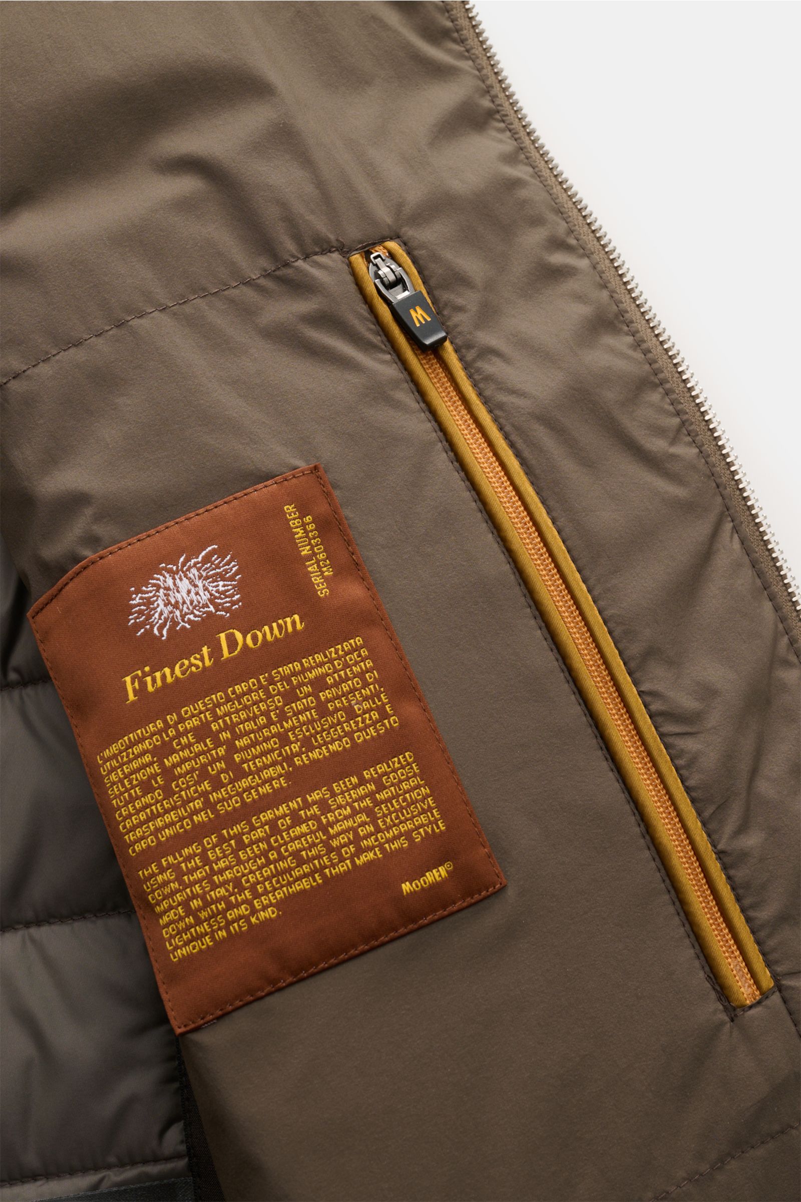Close-up inside view of the Moorer Daunenweste 'Calaf' dark olive showing a brown label with 'Finest Down' text and a yellow zipper pocket.

Description: Luxus in allerhöchster Qualität: Feinste sibirische Gänsedaunen werden für die gesteppte Outdoor-W