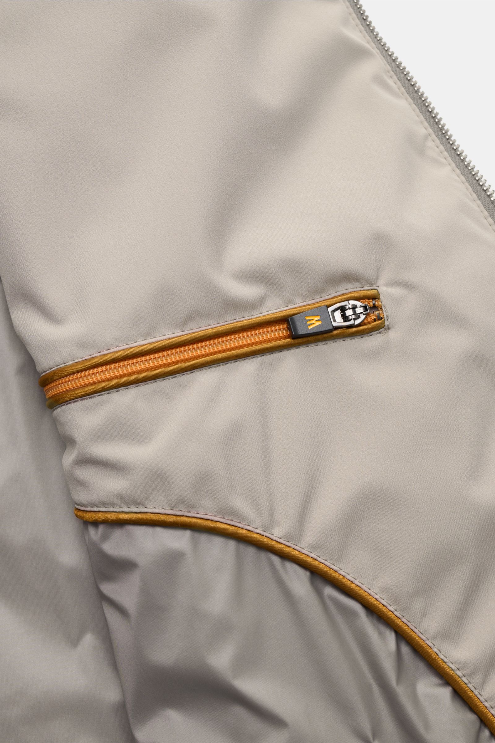 Close-up front detail of the beige Moorer Outdoor-Weste 'Senio-Skt,' showing water-repellent microfiber, smooth texture, slim fit, yellow zipper, and angled front pocket from a top-down perspective. The lightweight vest features light filling, a narrow st