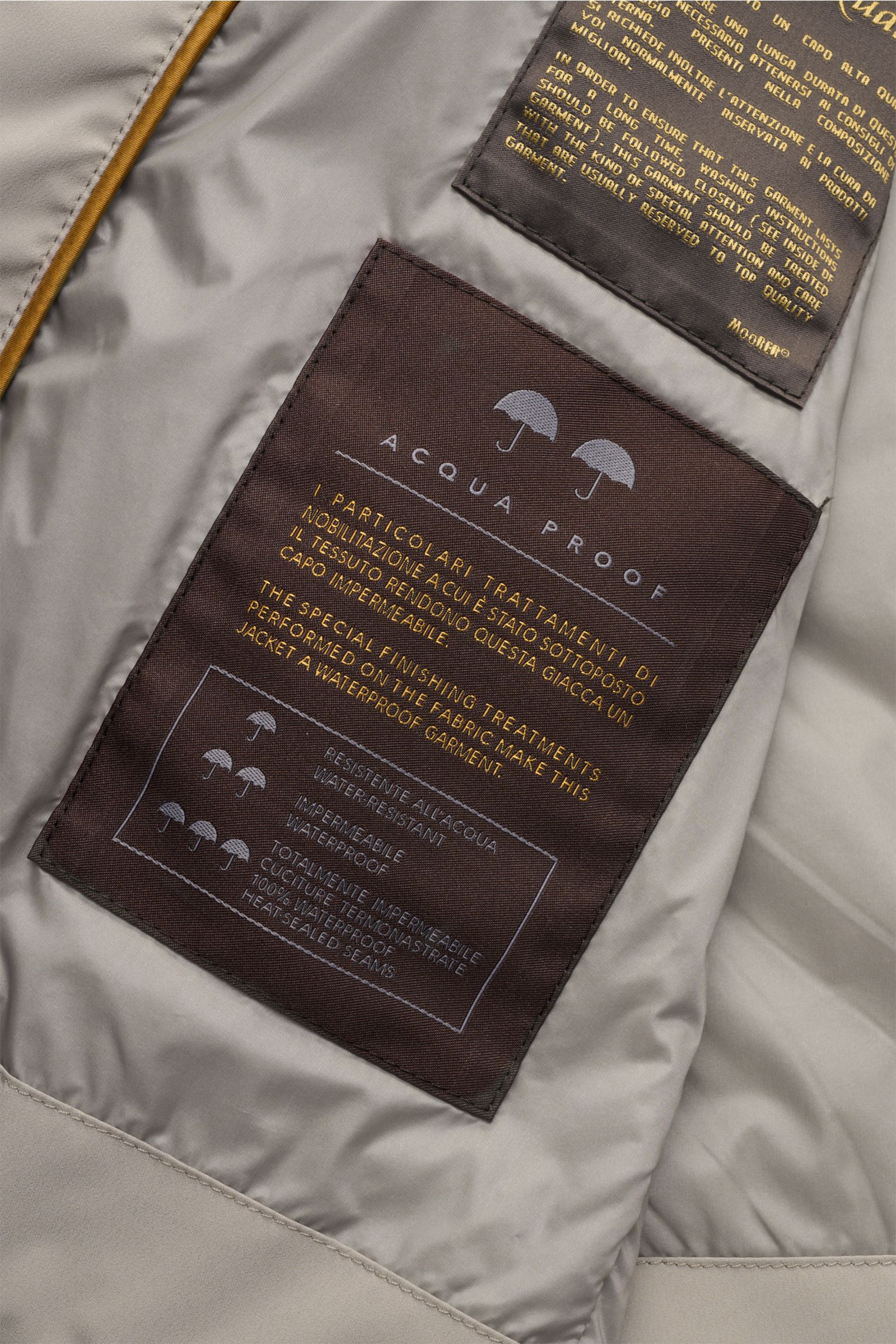 Close-up inside view of the beige Moorer Outdoor-Weste 'Senio-Skt' showing waterproof treatment labels and fabric details.

Description incorporating provided content:
Die leichte Outdoor-Weste 'Senio-Skt' von MOORER gehört in die Outerwear-Garderobe w