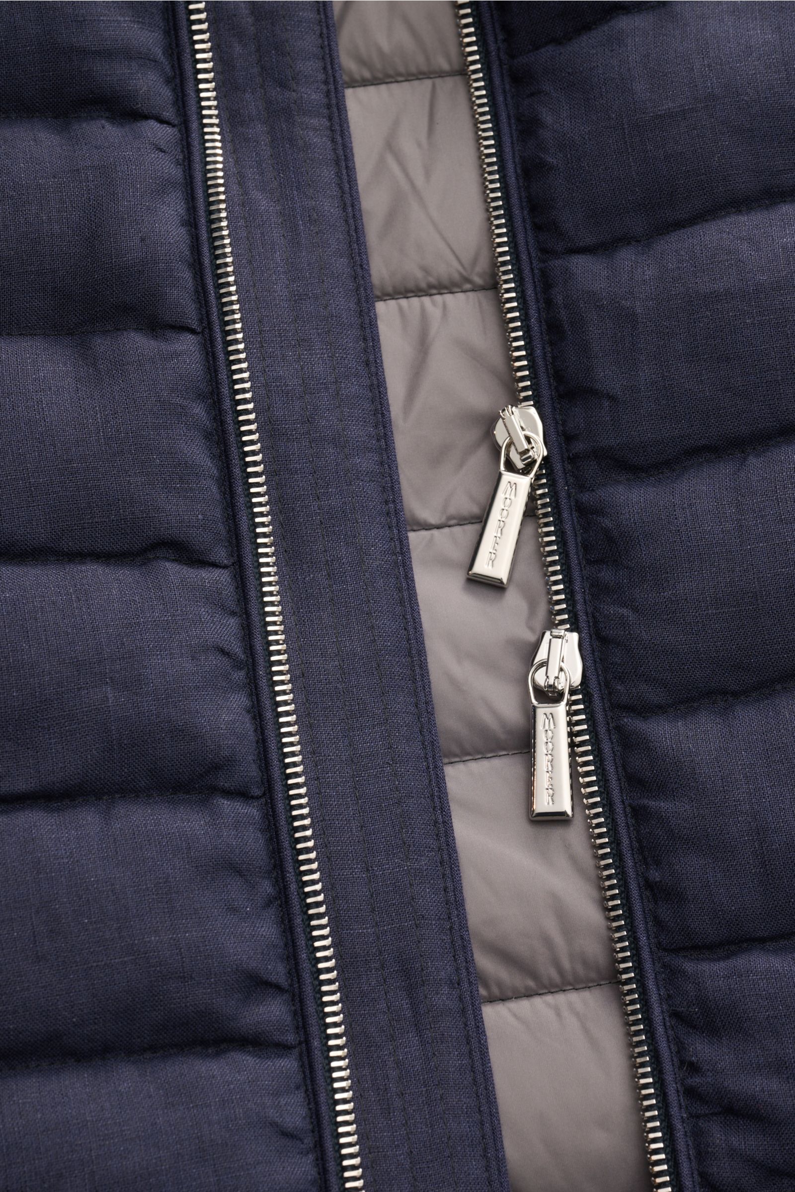 Close-up front view of the navy mottled Moorer Down gilet 'Calaf' showing its two-way silver zipper with branded pulls, narrow cross quilting, and soft linen fabric. Luxury of the very highest quality: Only the finest, hand-selected Siberian goose down is