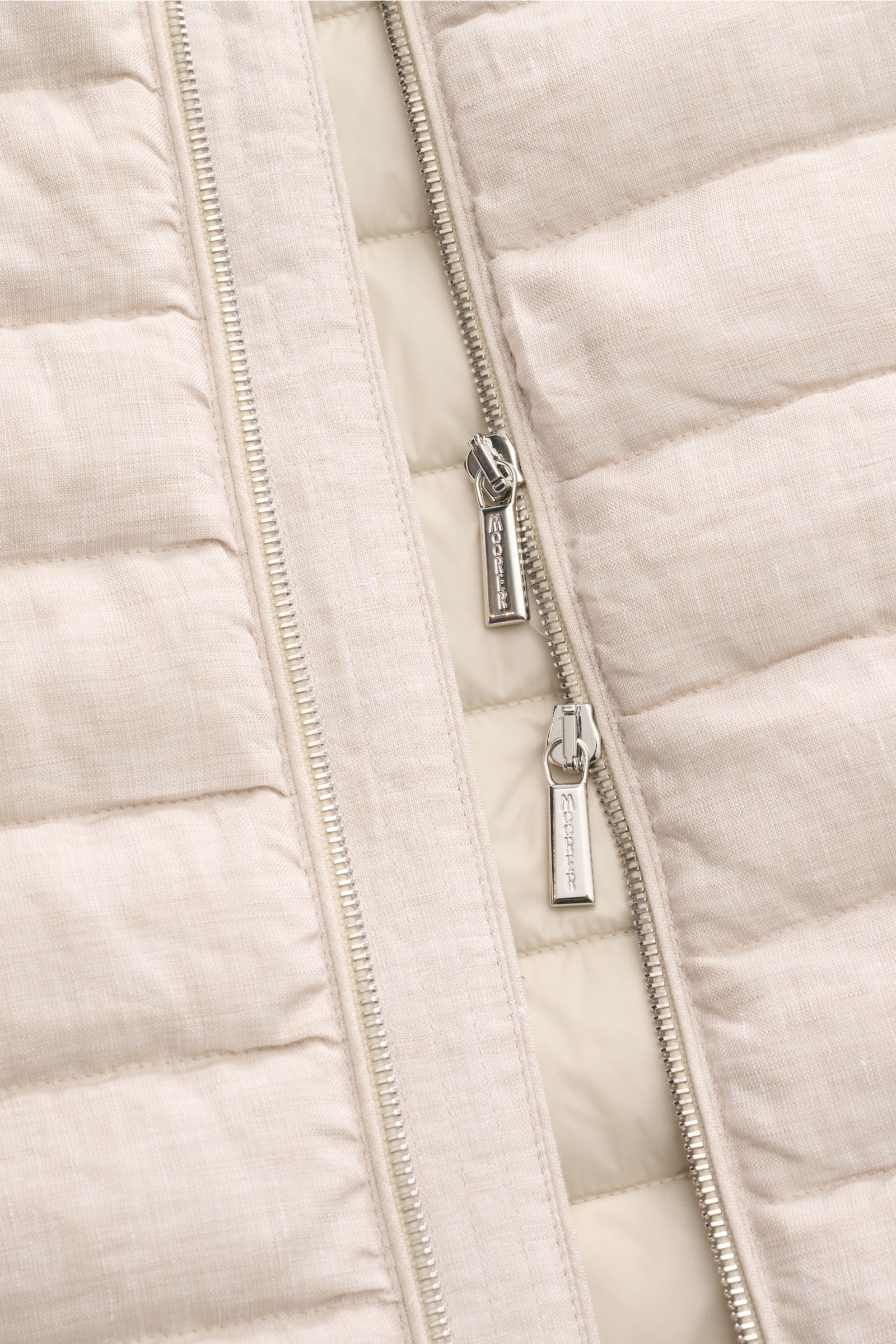Close-up front view of the beige mottled Moorer Down gilet 'Calaf' showing narrow cross quilting, two-way zip with branded pulls, and soft linen fabric texture. Luxury of the very highest quality: Only the finest, hand-selected Siberian goose down is used