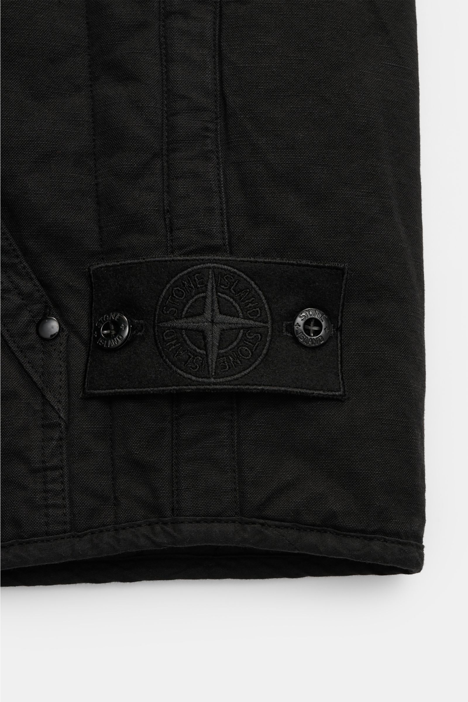 Alt-Tag (124 Zeichen): Nahaufnahme der Stone Island Outdoorweste 'Ghost Piece' schwarz mit tonalem Badge, Baumwoll-Leinen-Mix und Rippbündchen.