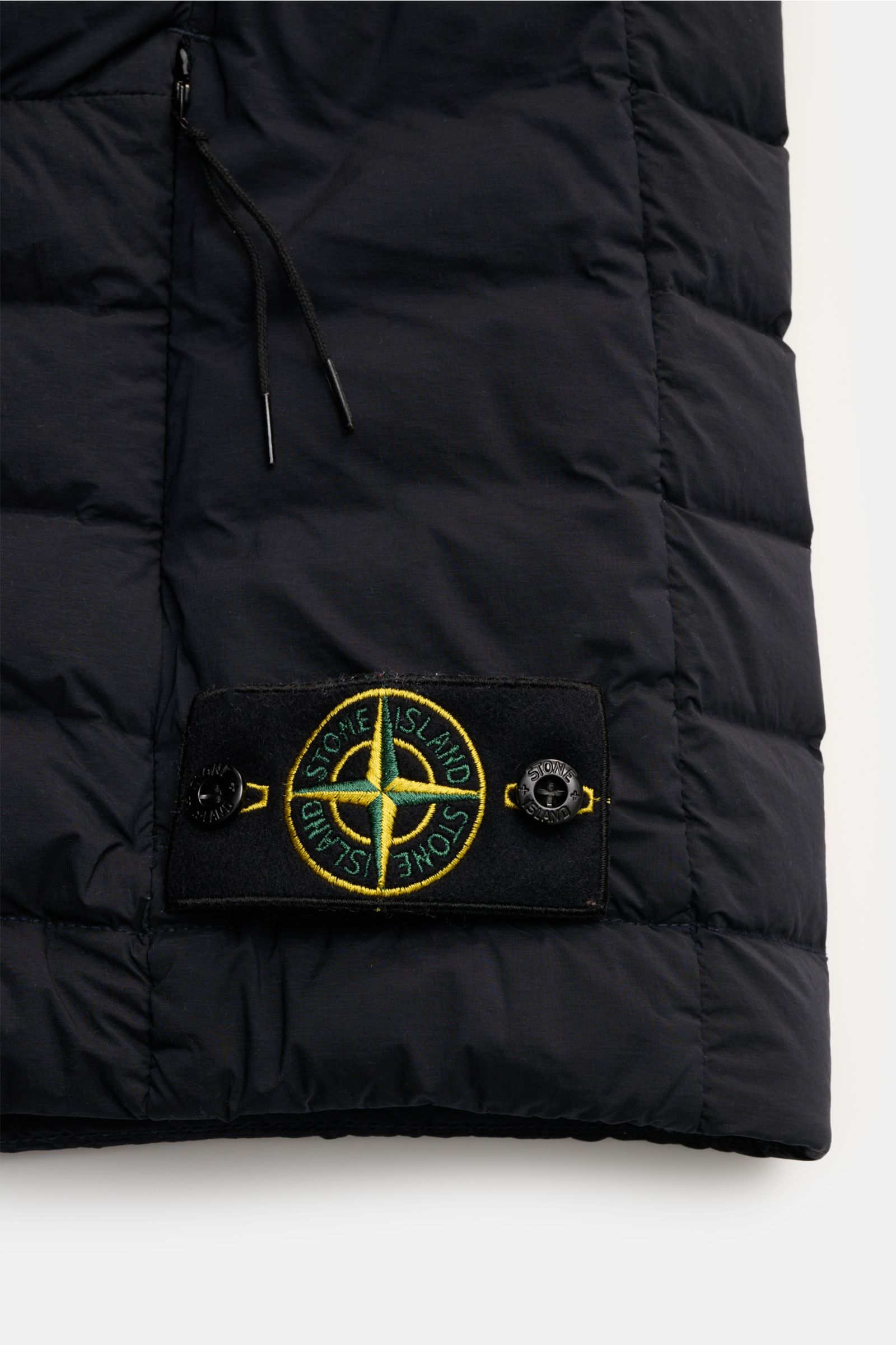 Close-up view of the lower front side of the Stone Island Daunenweste 'Seamless Tunnel Nylon Down' navy, showing the stitched logo patch with buttons on the padded, smooth microfiber fabric. Innovatives Outdoor Essential: Die STONE ISLAND Daunenweste b