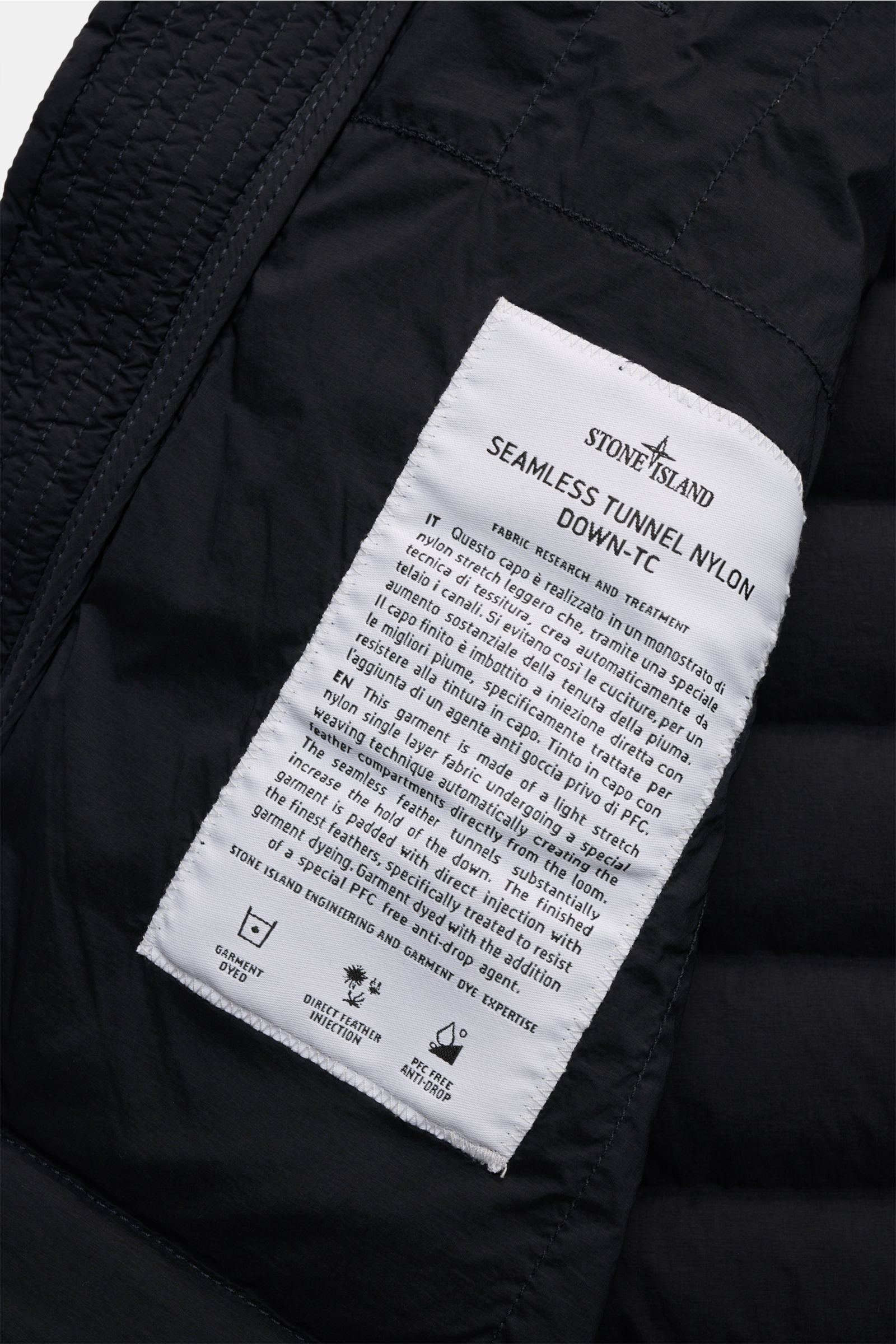 Close-up inside view of the Stone Island Daunenweste 'Seamless Tunnel Nylon Down' navy showing the white fabric label with detailed product information.

Description: Innovatives Outdoor Essential: Die STONE ISLAND Daunenweste besteht aus einem elastis