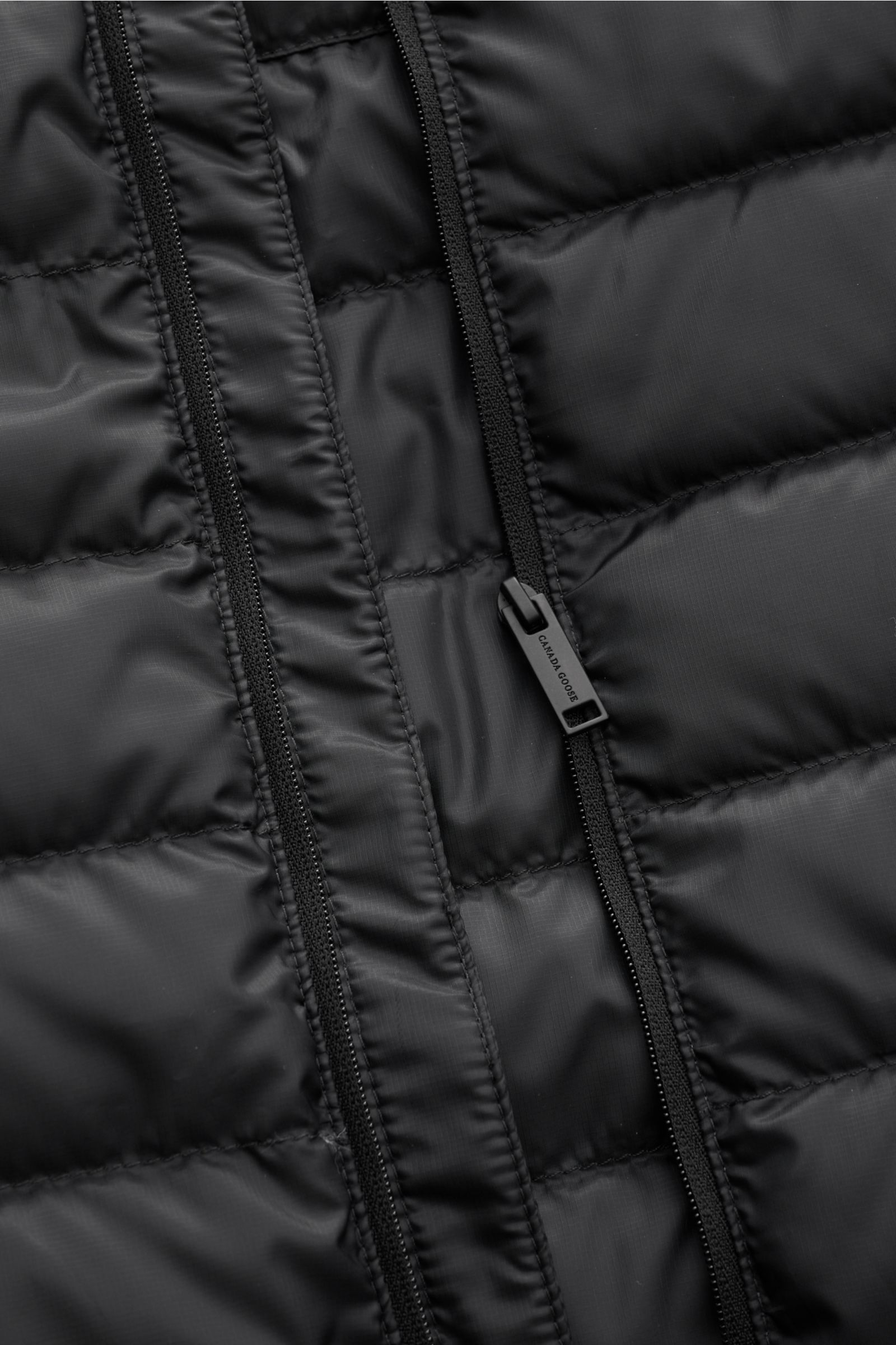 Nahaufnahme der Canada Goose Daunenweste 'Stratus Tonal' schwarz, zeigt Ripstop-Obermaterial, robusten Reißverschluss und glatten Griff frontal.