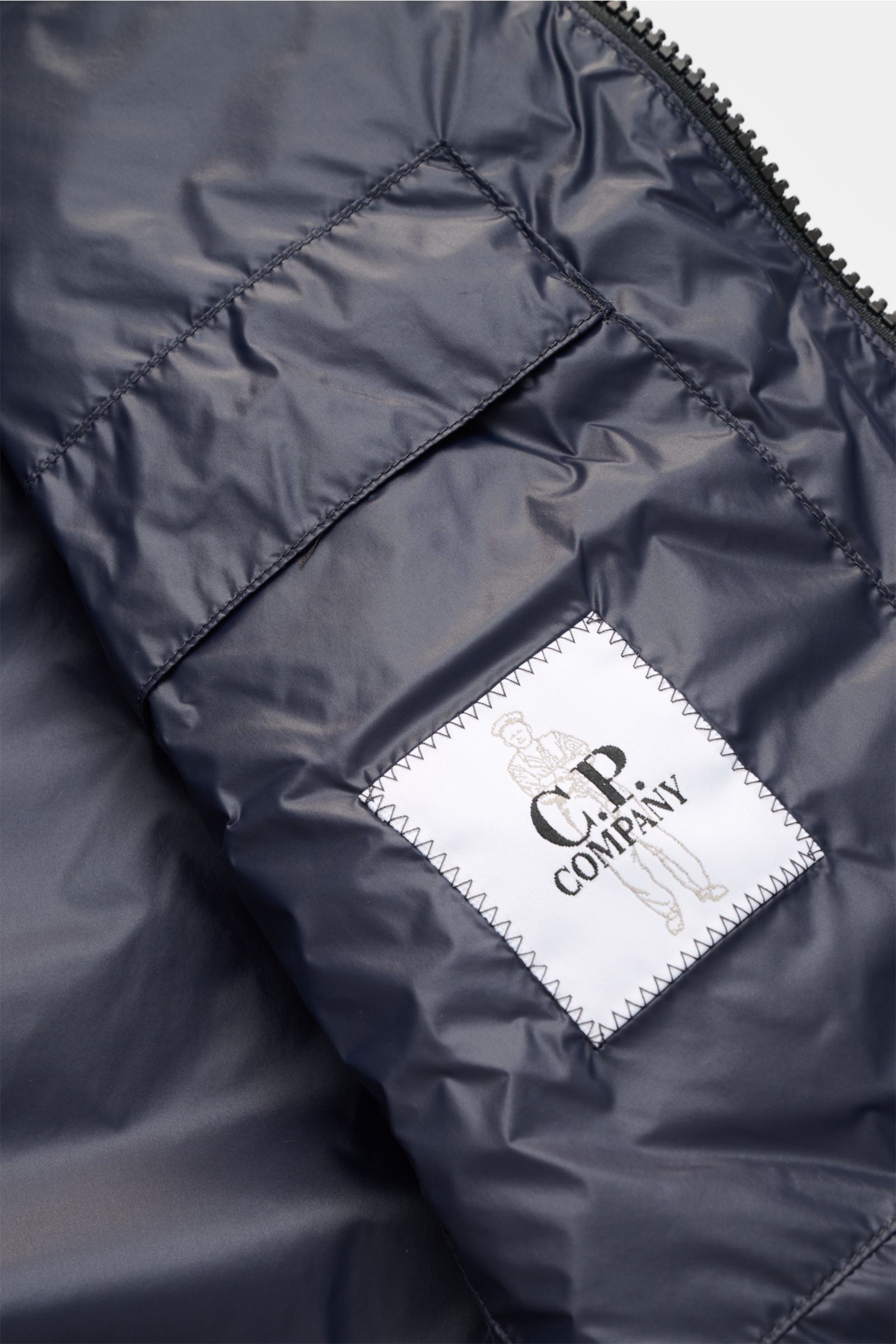 Close-up of the inner pocket and label of the C.P. Company Daunenweste 'D.D. Shell' dark navy photographed from inside, showing smooth, water-repellent Ripstop microfiber. Die Konstruktion der Daunenweste 'D.D. Shell' von C.P. COMPANY zeichnet sich dur