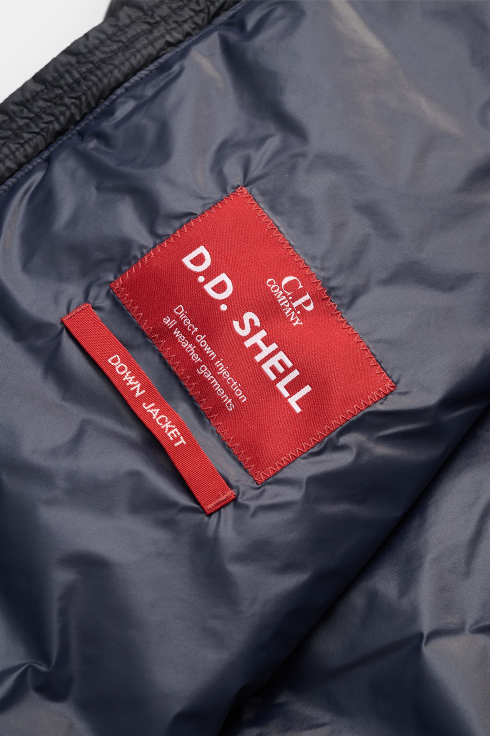 Close-up image of the inside lining and red label of the C.P. Company Daunenweste 'D.D. Shell' dark navy, photographed from a top-down perspective. Die Konstruktion der Daunenweste 'D.D. Shell' von C.P. COMPANY zeichnet sich durch ihre besondere Qualität 