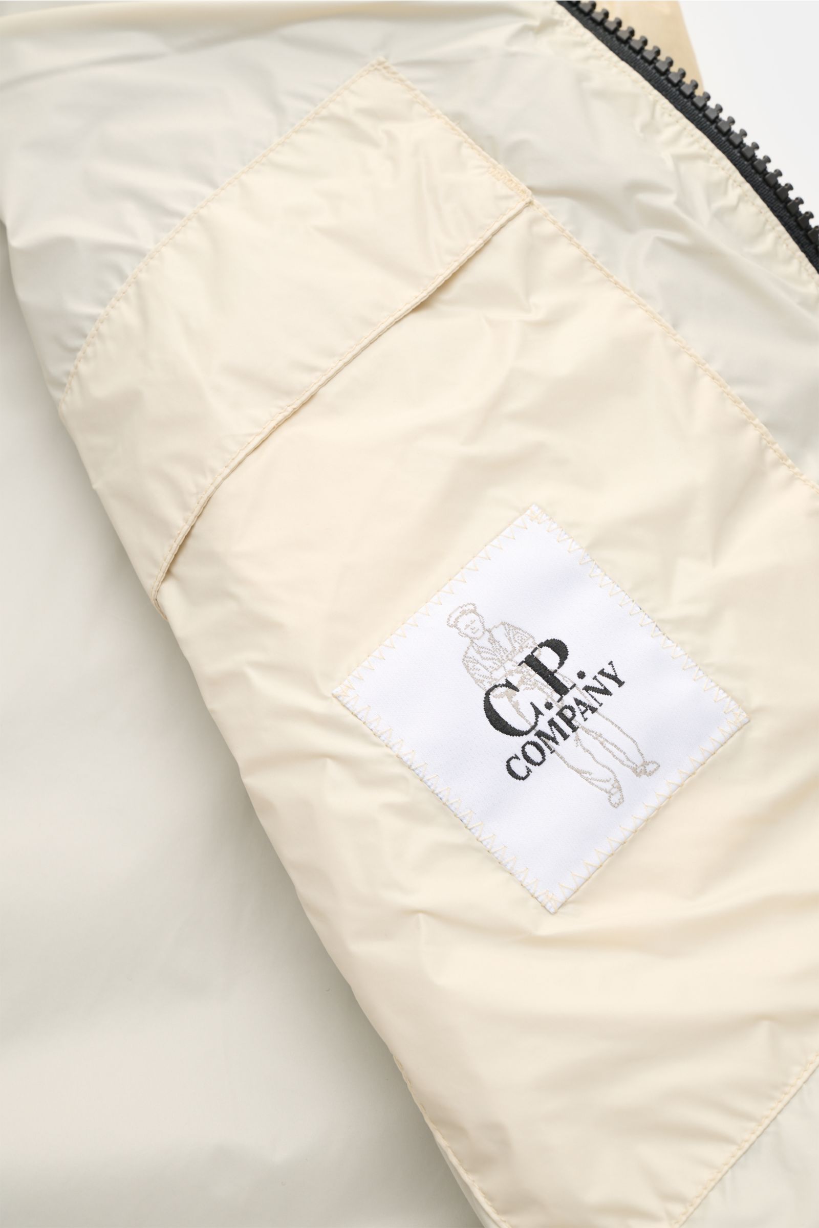 Close-up inside view of C.P. Company Daunenweste 'D.D. Shell' beige showing smooth ripstop microfiber lining and branded label.

Description incorporating provided content: The image shows a close-up inside view of the C.P. Company Daunenweste 'D.D. Shell