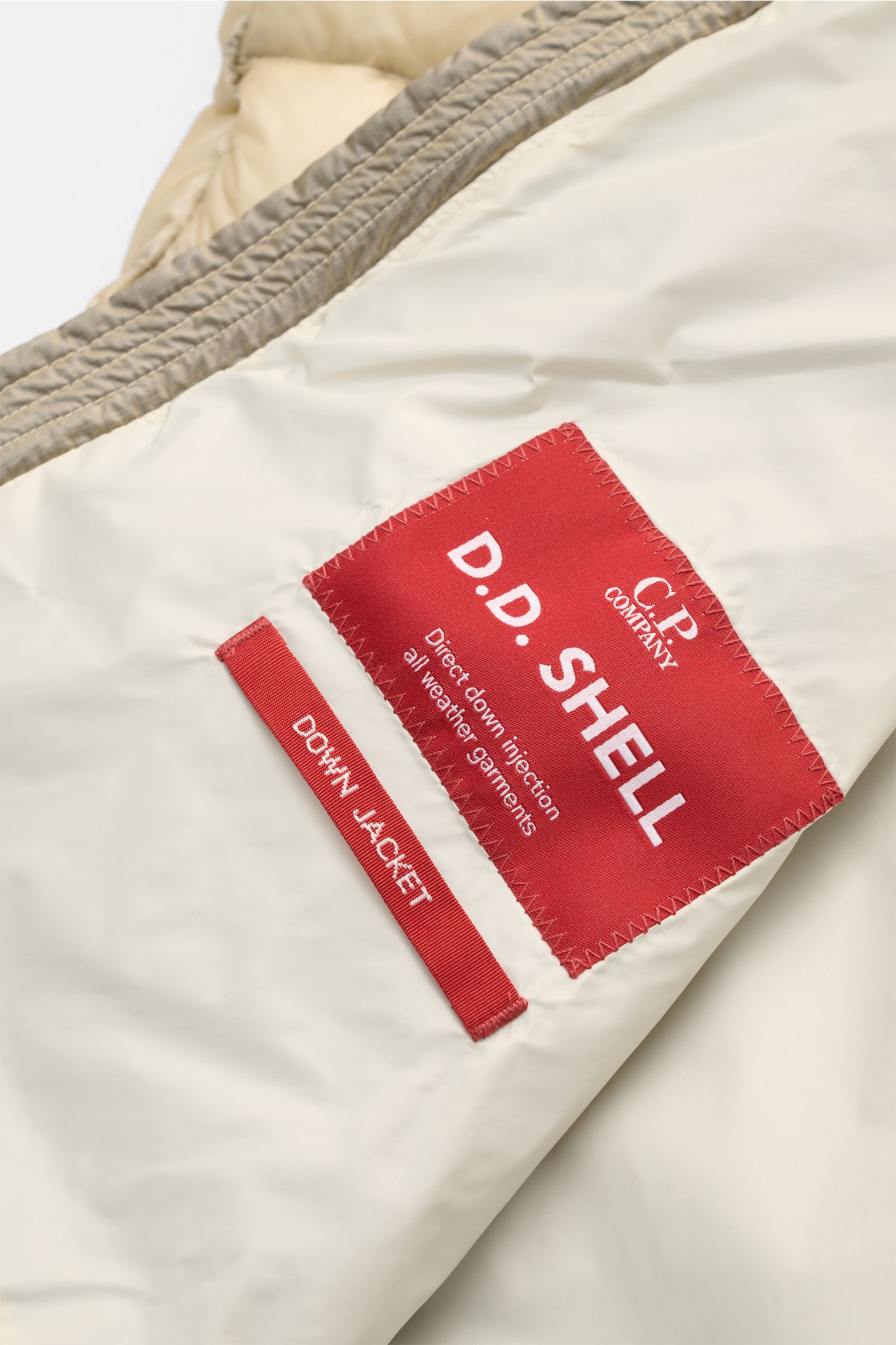 Close-up inner view of C.P. Company Daunenweste 'D.D. Shell' beige showing red label and smooth fabric, highlighting quality and design.