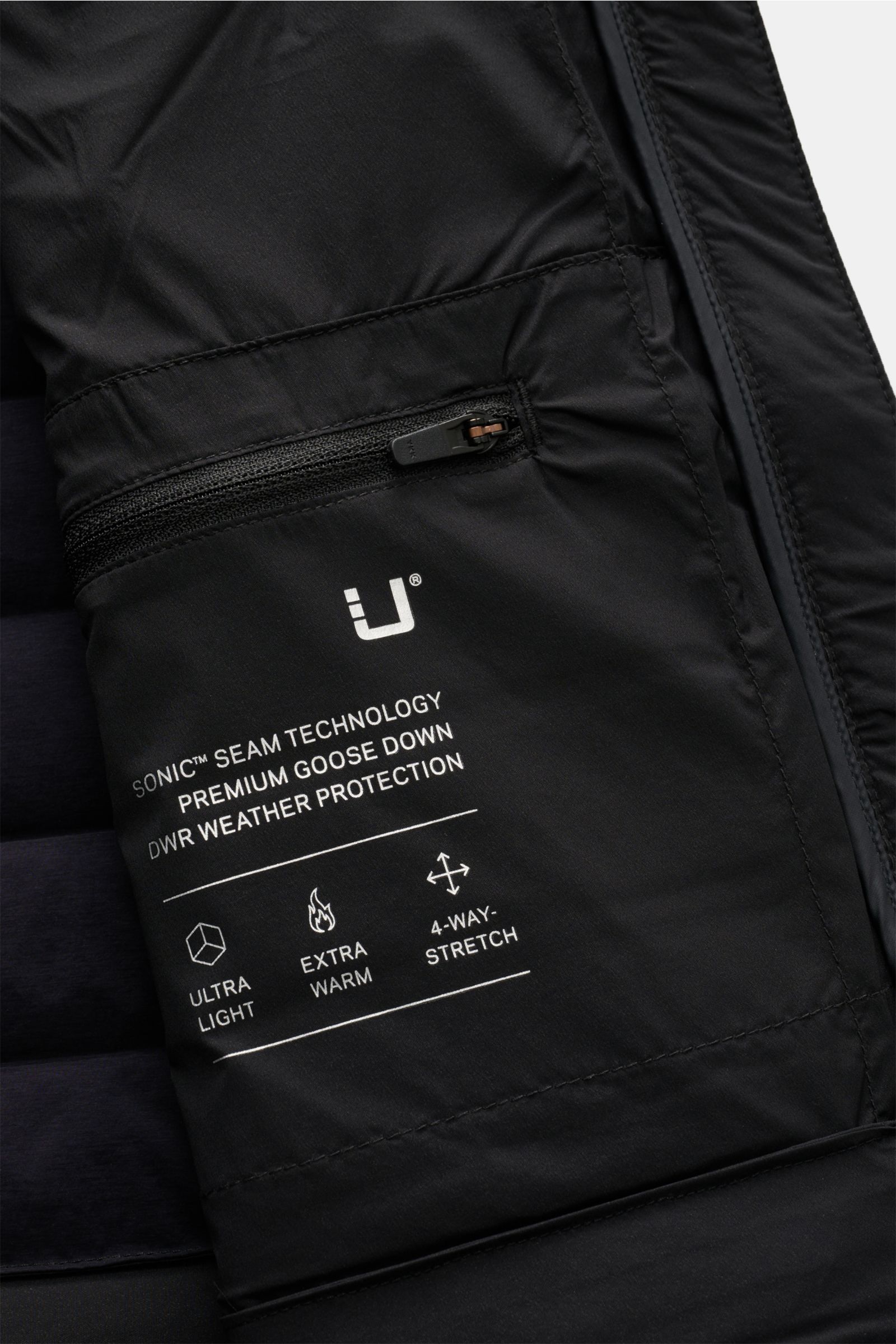 Close-up interior view of the UBR Daunenweste 'Supersonic' navy showing a zipped inner pocket with white printed text detailing sonic seam technology, premium goose down, DWR weather protection, ultra light, extra warm, and 4-way stretch features.