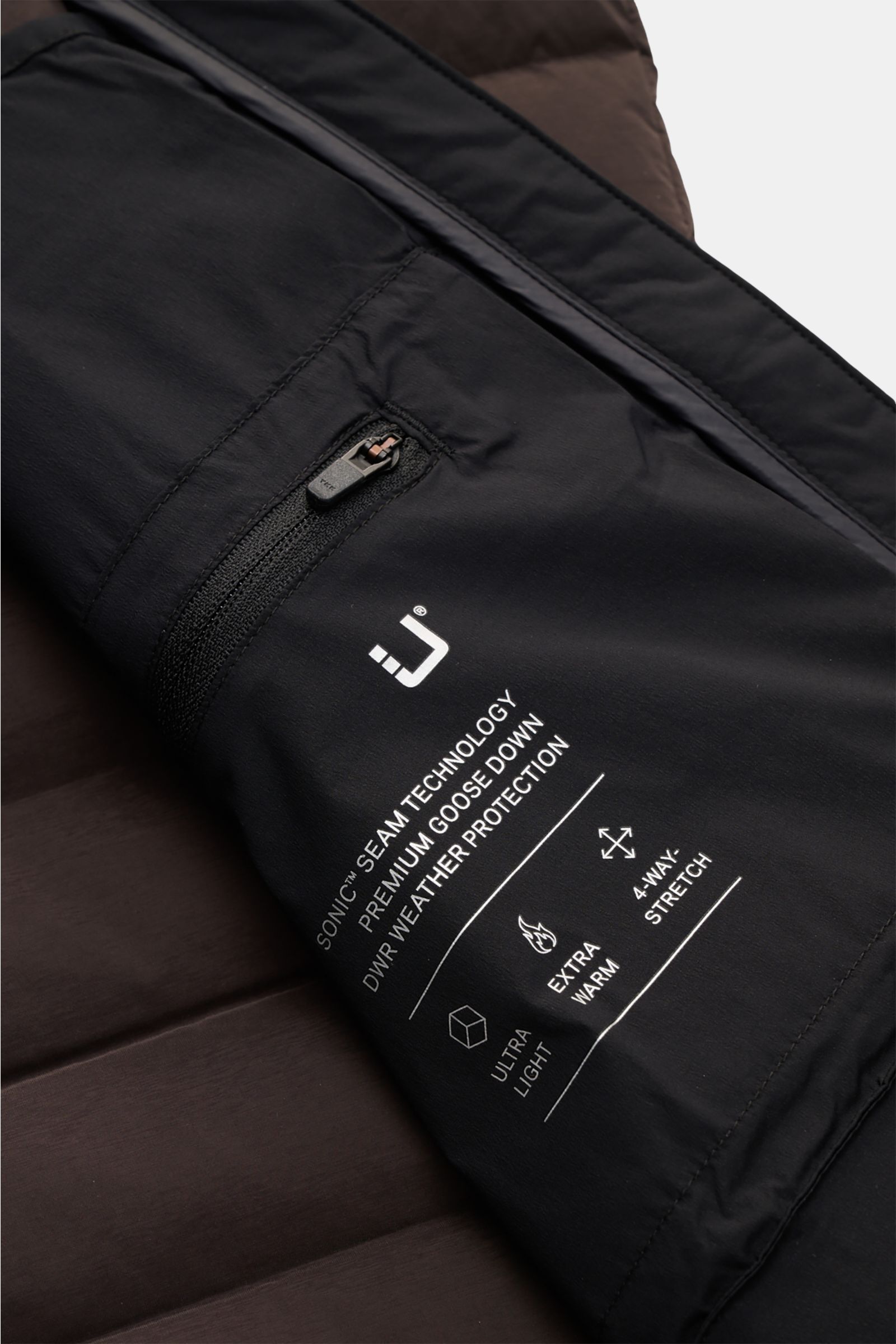 UBR Down gilet 'Supersonic' grey-brown close-up from above showing black sleeve with zip pocket, logo, and tech details on dark fabric.