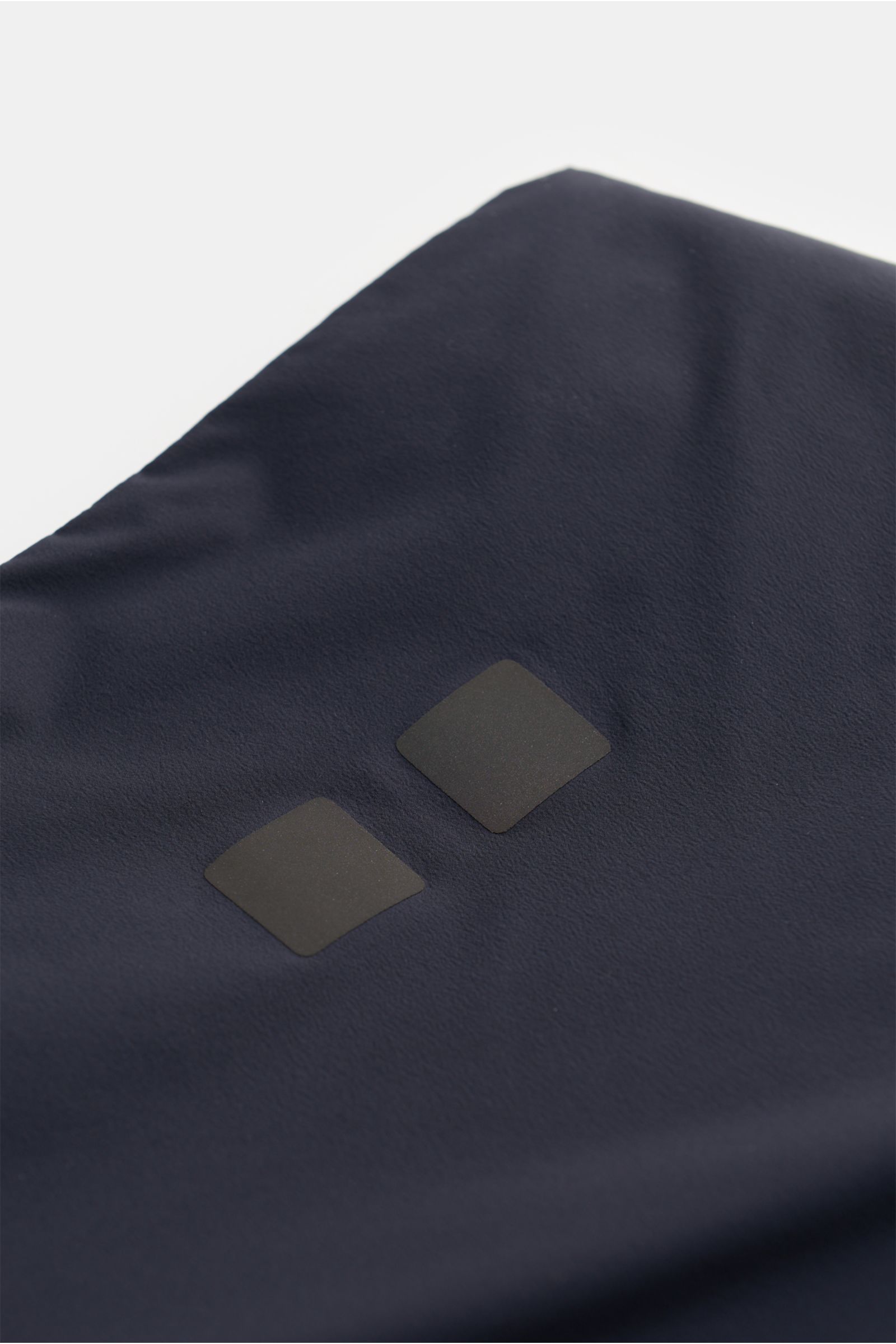 Close-up detail of the navy fabric and reflective logo print of the UBR Outdoor-Weste 'Raptor' navy, photographed from above. Leichtigkeit, die man spürt – Performance, die bleibt: Mit der Weste 'Raptor' zeigt UBR, wie moderne Essentials aussehen. Ob wärm