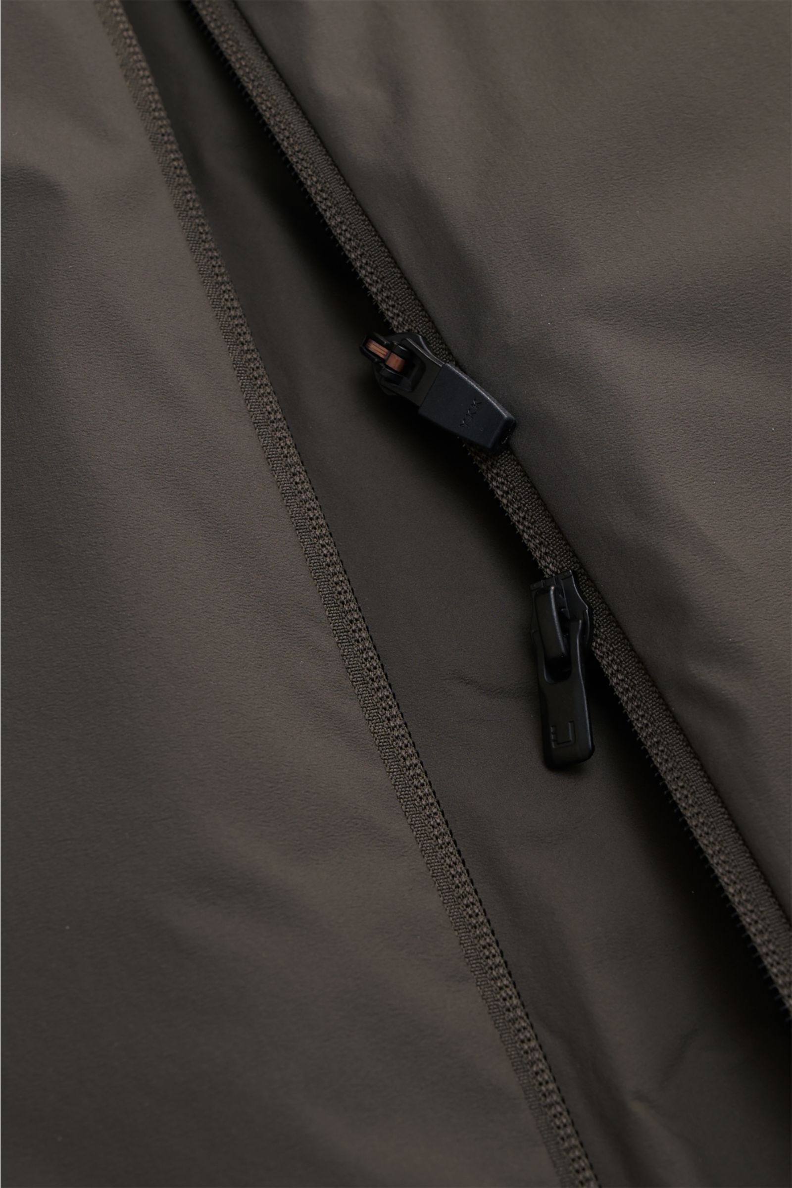 Nahaufnahme der UBR Outdoor-Weste 'Raptor' oliv mit hochwertiger Microfaser, leicht wattiert, zwei-Wege-Reißverschluss aus schräger Perspektive.