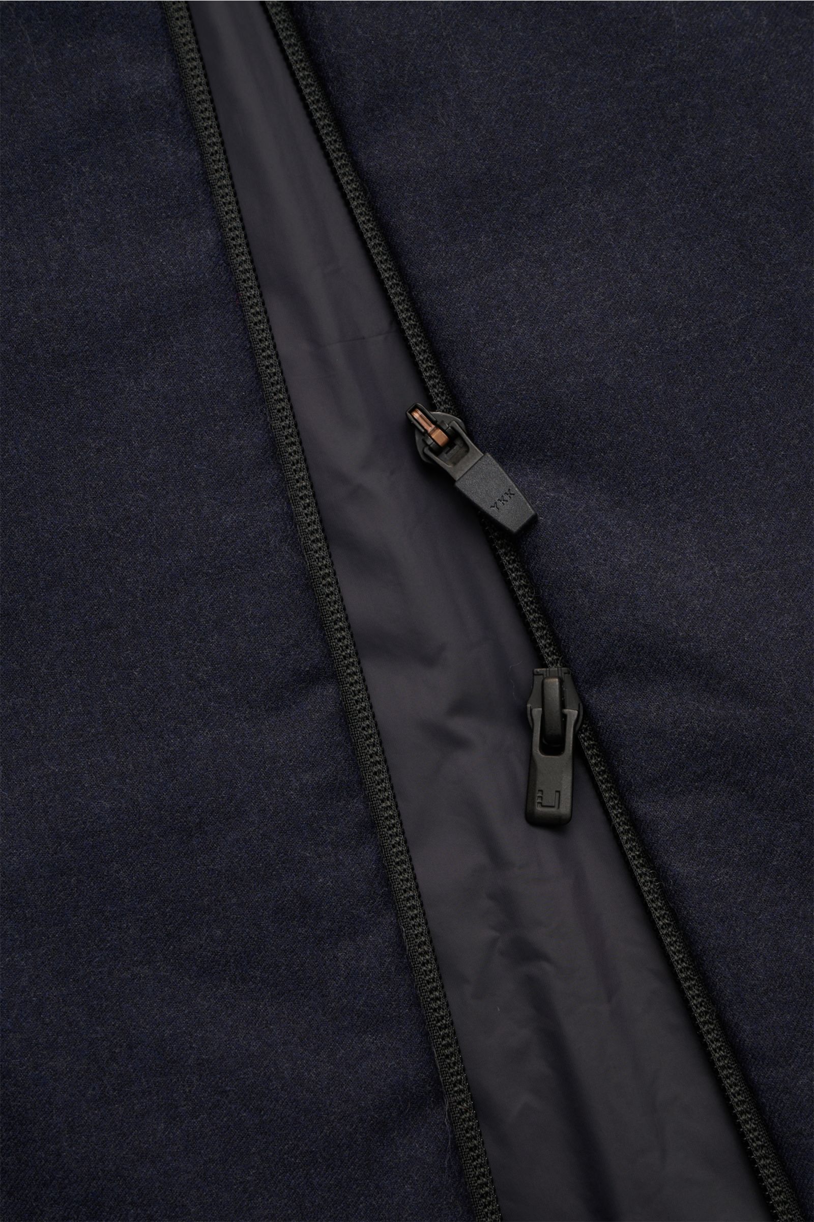 Close-up image from a top-down perspective showing the two-way zipper detail of the UBR Outdoorweste 'Raptor Savile' navy meliert. Funktion trifft zeitloses Design: Die 'Raptor Savile' Weste von UBR bietet mit ihrer leichten Wattierung optimalen Komfort i