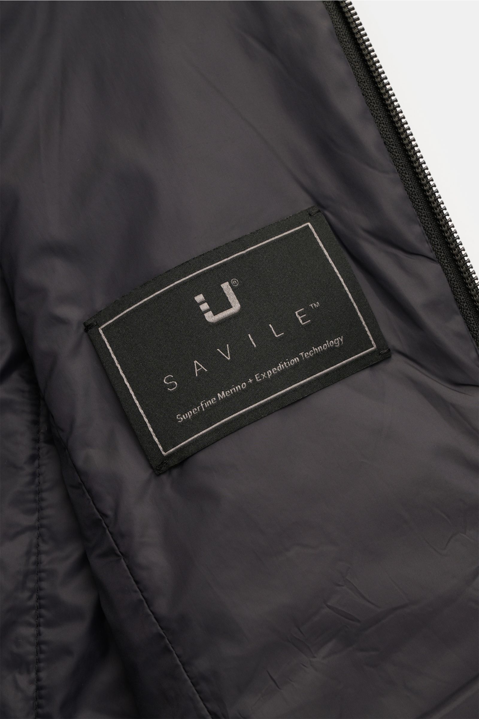 Nahaufnahme des Innenfutters der UBR Outdoorweste 'Raptor Savile' anthrazit mit Markenlabel, geschmeidiger Stoff, Zwei-Wege-Reißverschluss sichtbar.