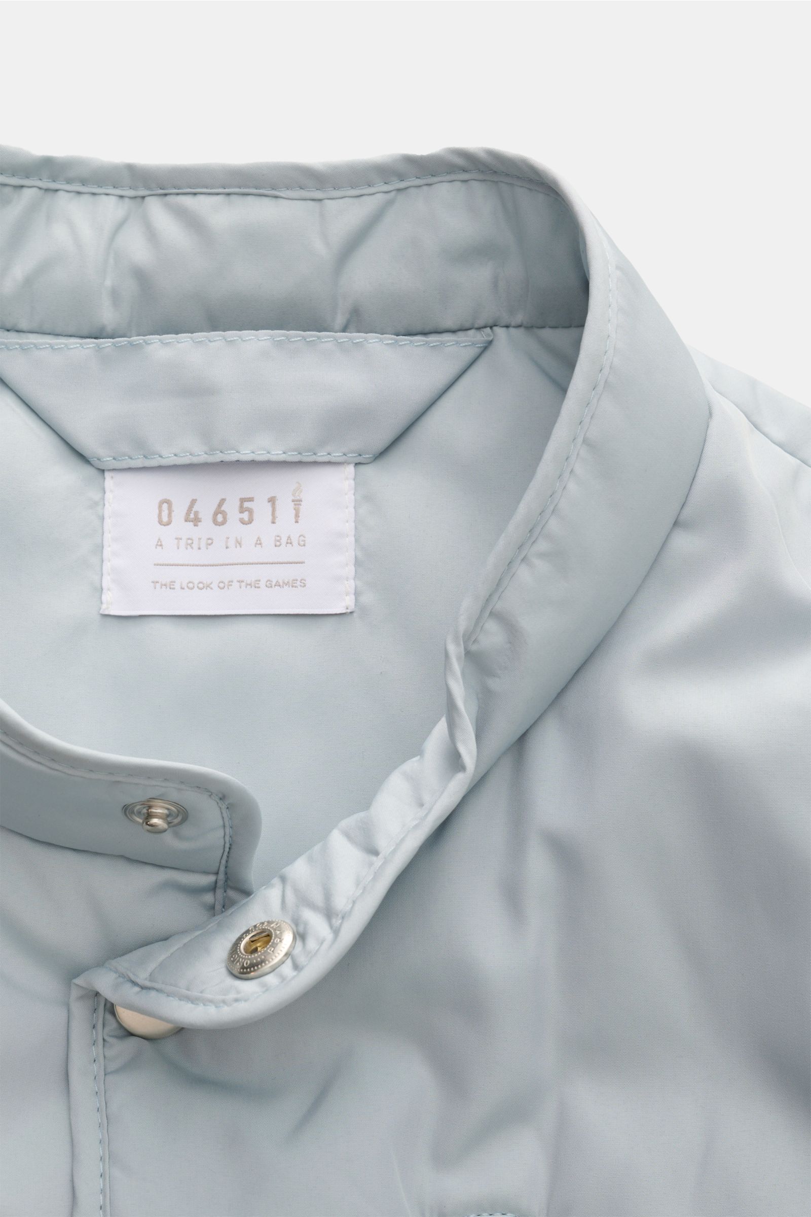 Close-up front view of the collar and label of the 04651/ A trip in a bag Outdoor Weste 'MC26' hellgrau, made of high-quality microfiber with a smooth touch and light padding. Inspiriert von den Olympischen Winterspielen in Cortina und Mailand, legt diese
