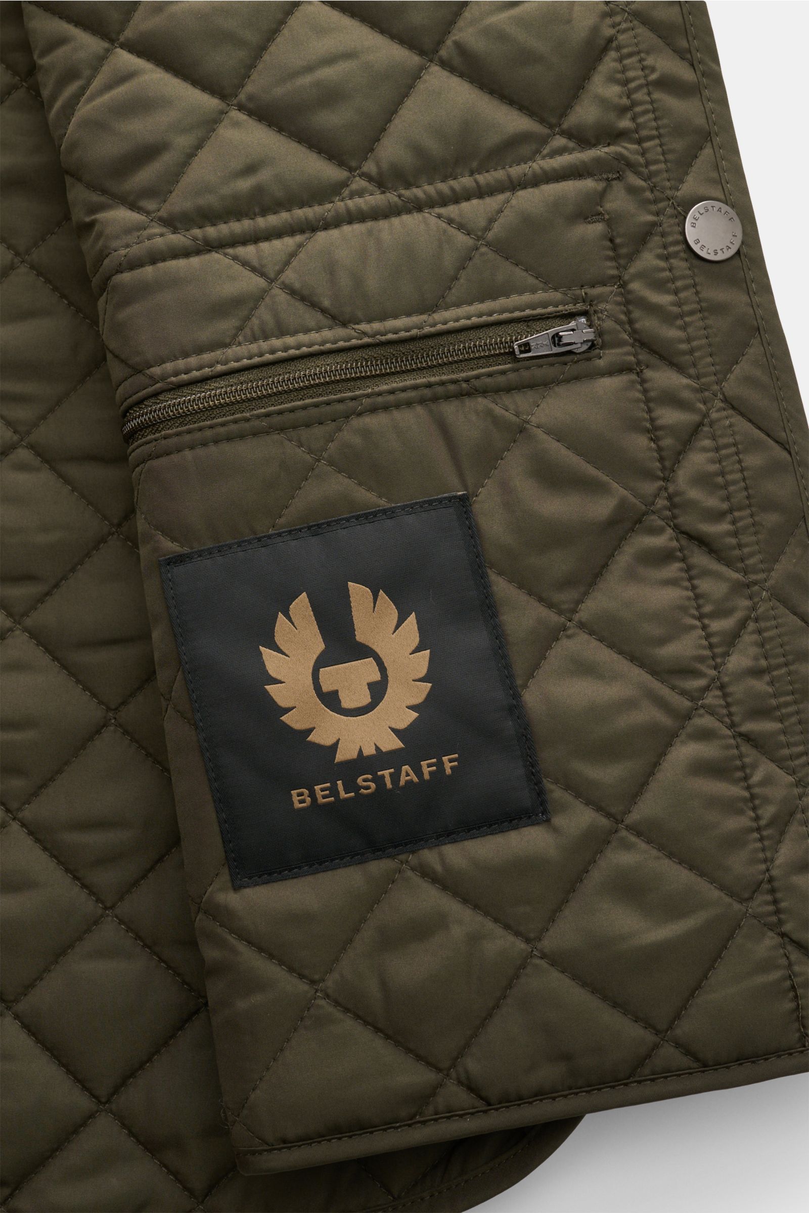 Nahaufnahme der Belstaff Outdoorweste 'Icon' dark olive von innen, mit Steppung, Innenreißverschluss, BELSTAFF-Logo und Druckknopfverschluss.