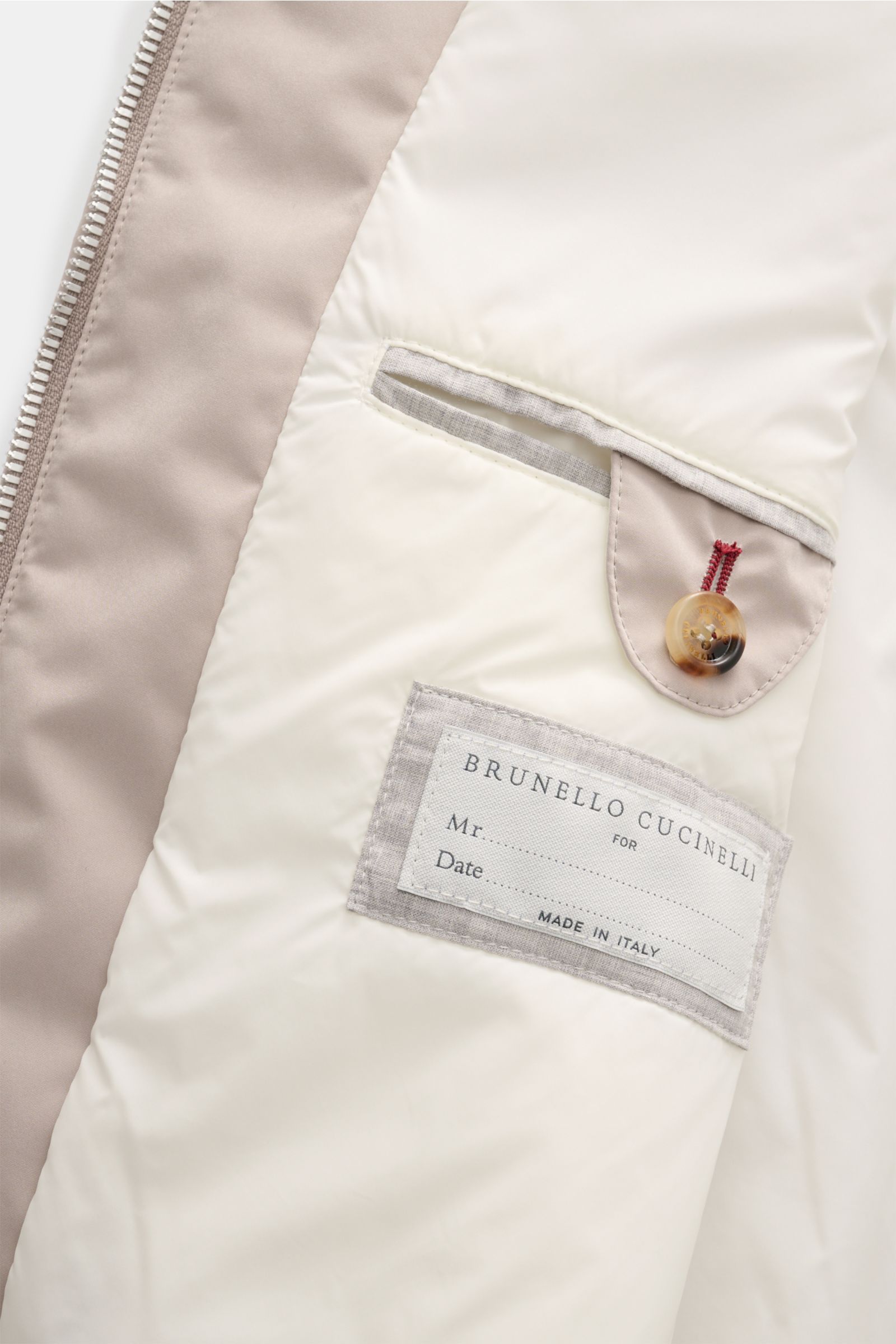 Nahaufnahme der Innenseite der Brunello Cucinelli Outdoorweste beige, fotografiert von oben, mit weichem Futter, Innentaschen und Label.