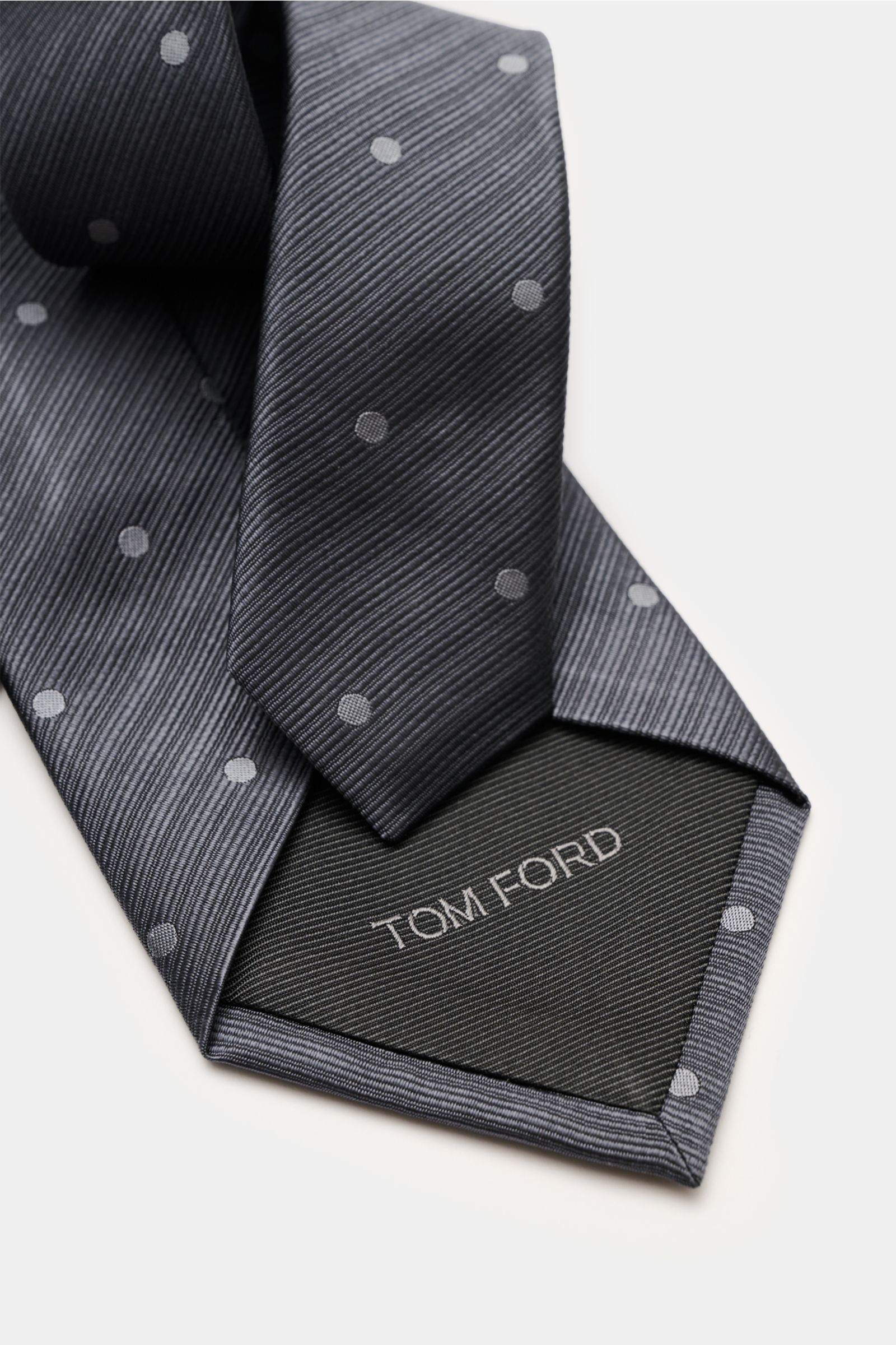 Tom Ford Seidenkrawatte in dark gray with subtle dots, silk texture, logo stitching, photographed from a close angle.