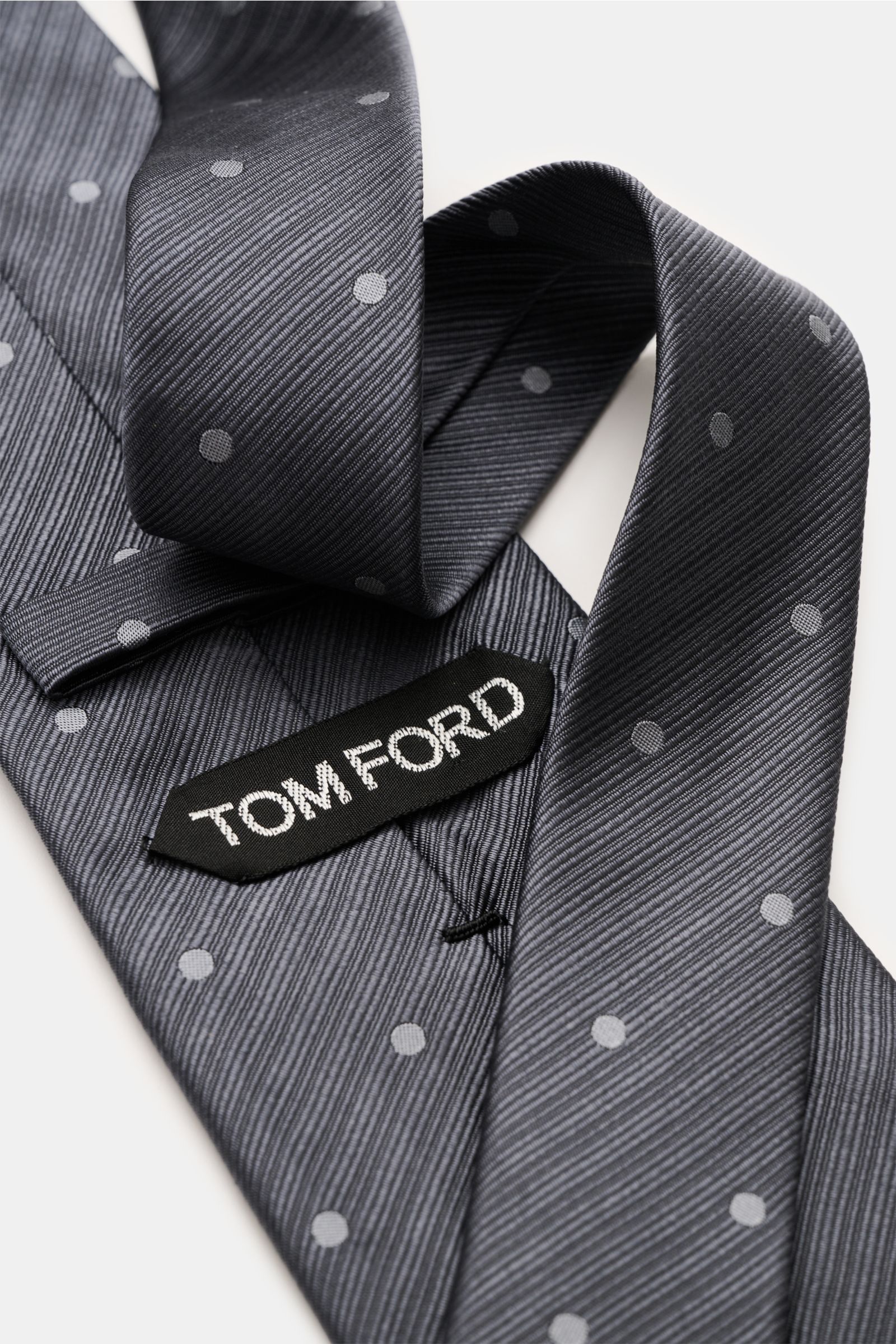 Close-up of a Tom Ford Seidenkrawatte, dark grey with dots, silk, subtle shine, logo stitching, made in Italy.
