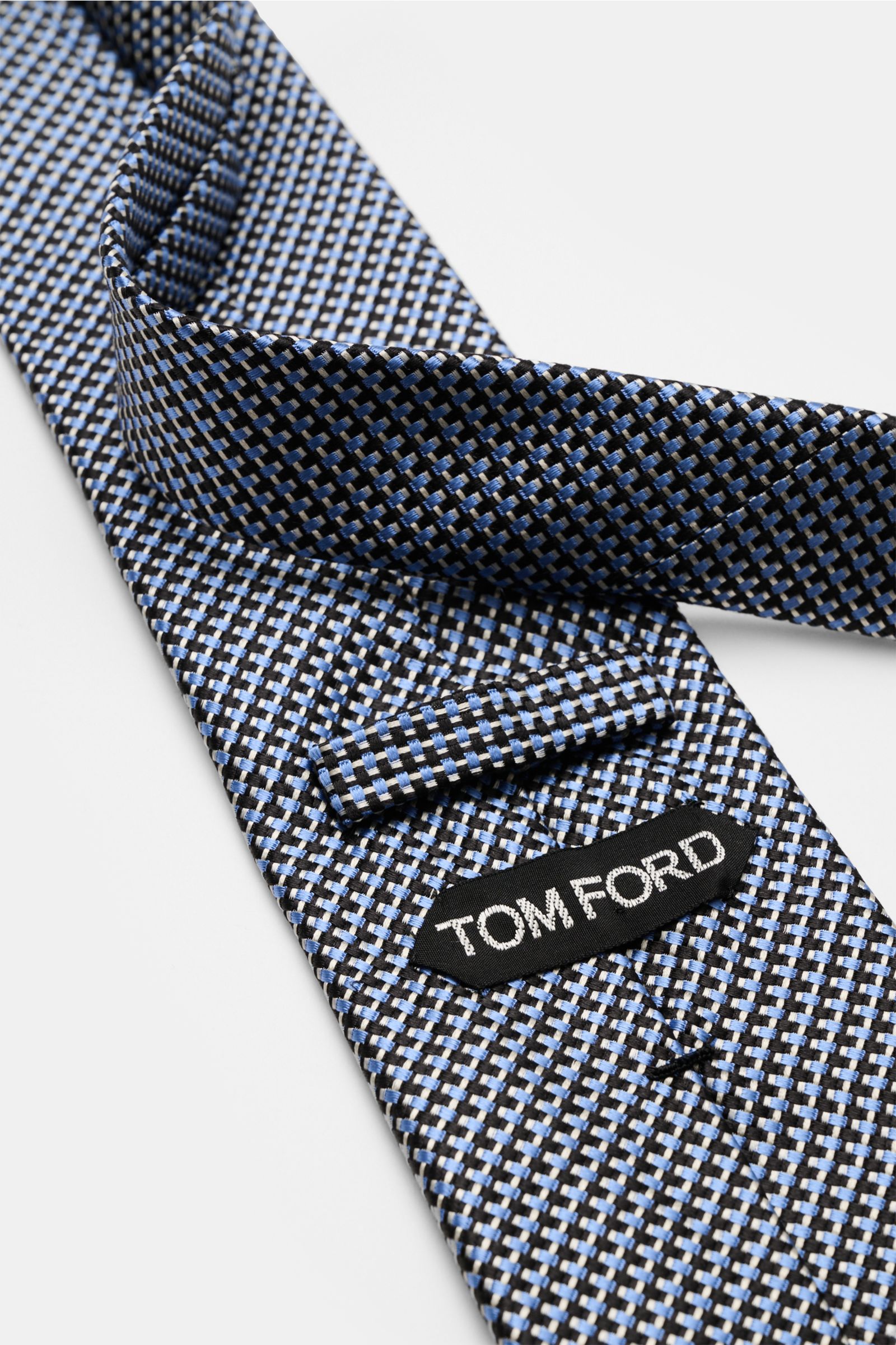 Close-up front view of the Tom Ford Seidenkrawatte hellblau/schwarz/grau gemustert showing its fine woven pattern and branded label on pure silk.

Italienische Handwerkskunst: Dieser Krawatten-Klassiker von TOM FORD aus reiner Seide vereint zeitlose El