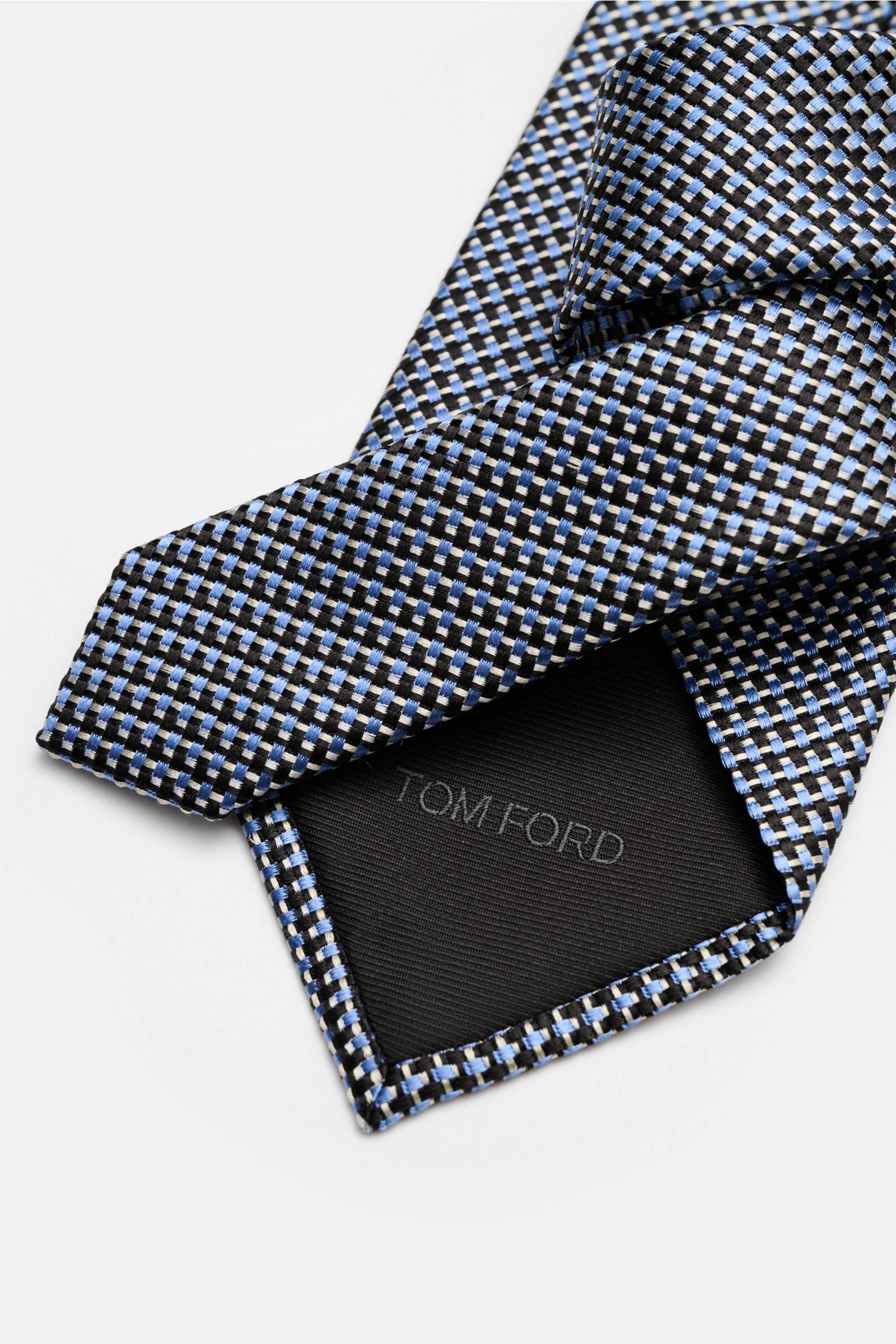 Alt tag (125 characters max):  
Close-up view of Tom Ford Seidenkrawatte hellblau/schwarz/grau gemustert showing fine silk weave and branded lining.

Detailed description for image context:  
Italienische Handwerkskunst: Dieser Krawatten-Klassiker von 