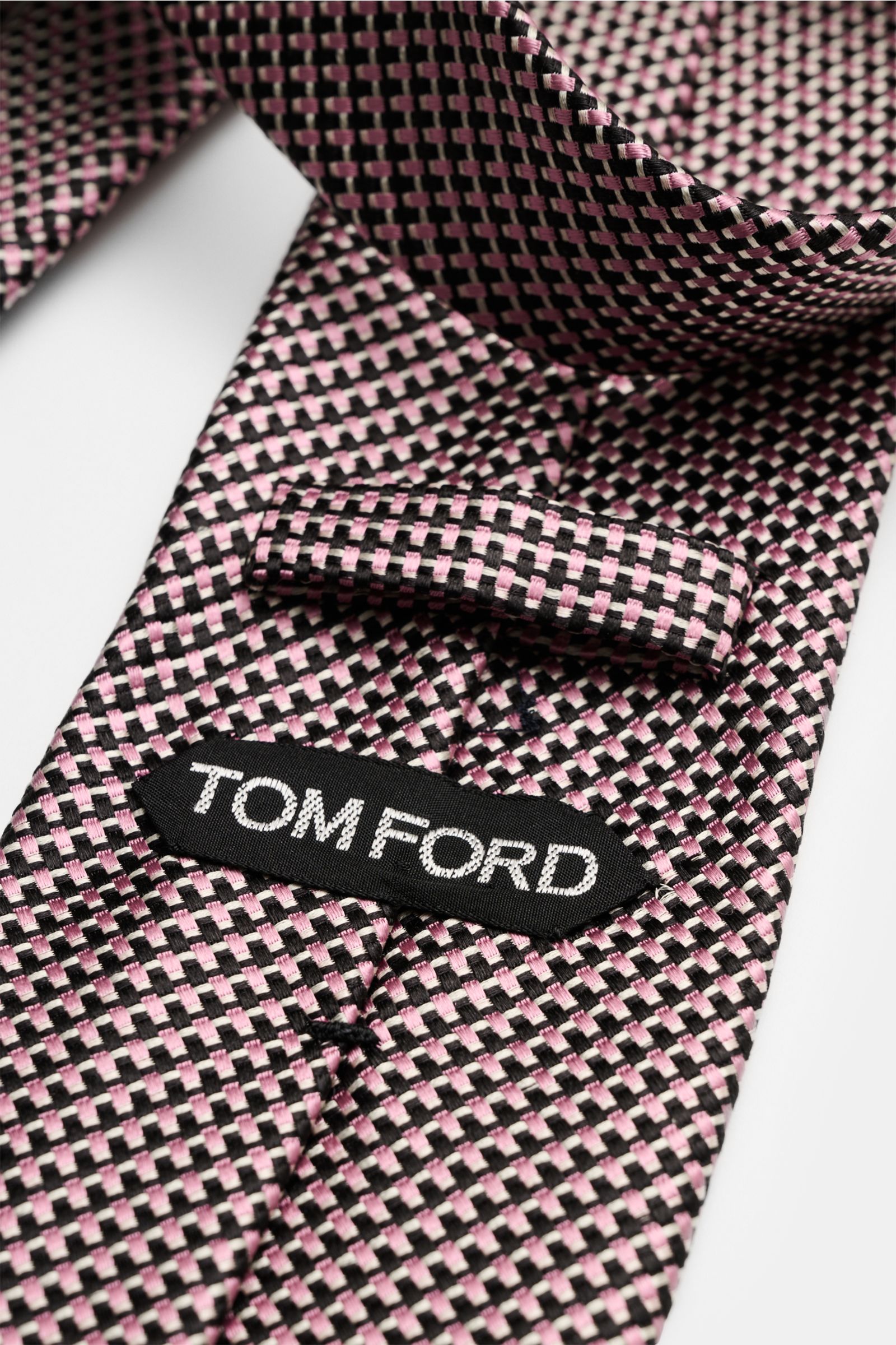 Close-up view of the Tom Ford Seidenkrawatte rosé/schwarz/grau gemustert showcasing its fine graphic weave and branded label.  
Italienische Handwerkskunst: Dieser Krawatten-Klassiker von TOM FORD aus reiner Seide vereint zeitlose Eleganz mit einem fei