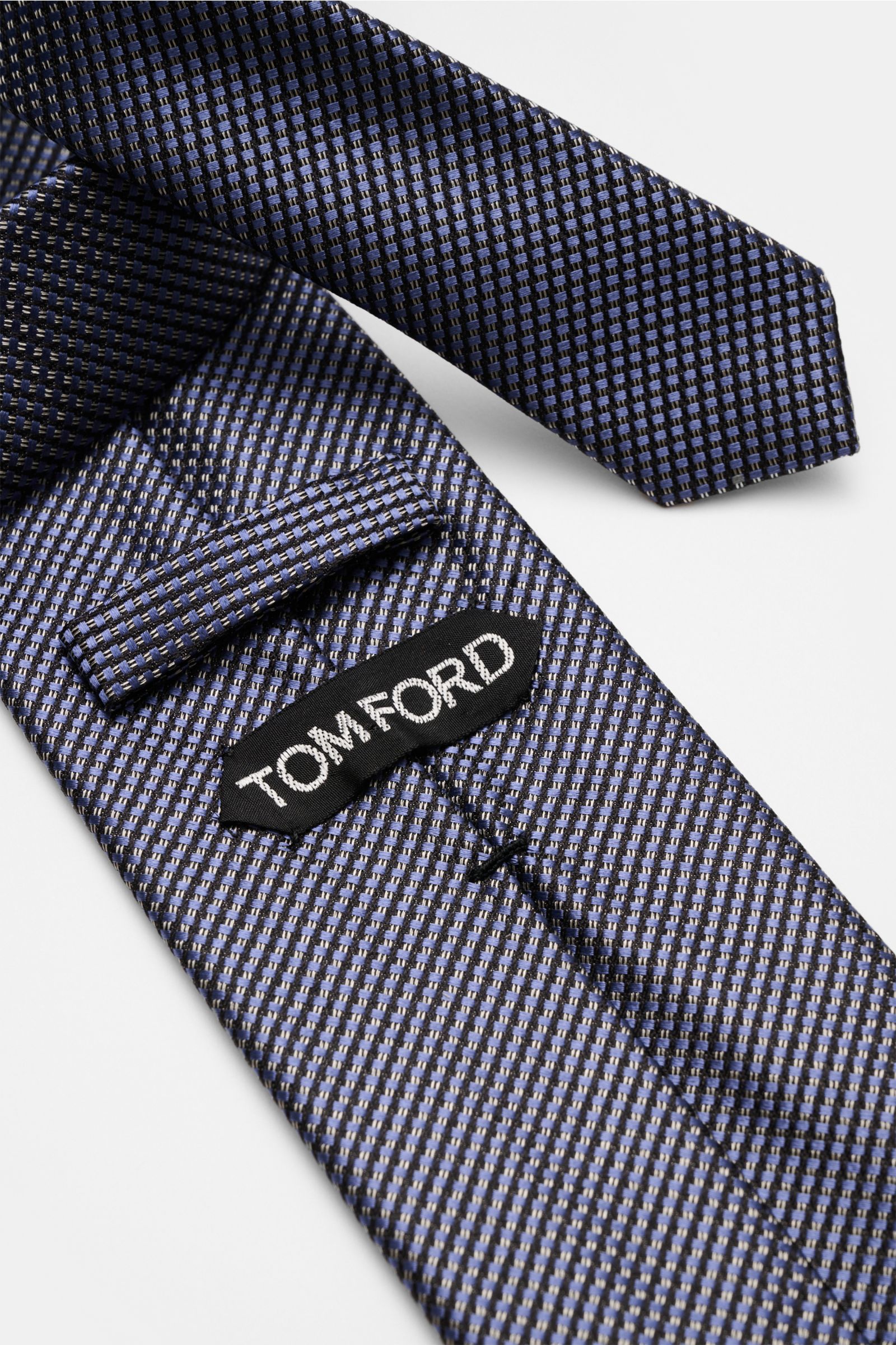 Close-up top view of Tom Ford Seidenkrawatte rauchblau/schwarz/grau gemustert showing fine silk weave, subtle shine, and branded lining. Italienische Handwerkskunst: Dieser Krawatten-Klassiker von TOM FORD aus reiner Seide vereint zeitlose Eleganz mit 