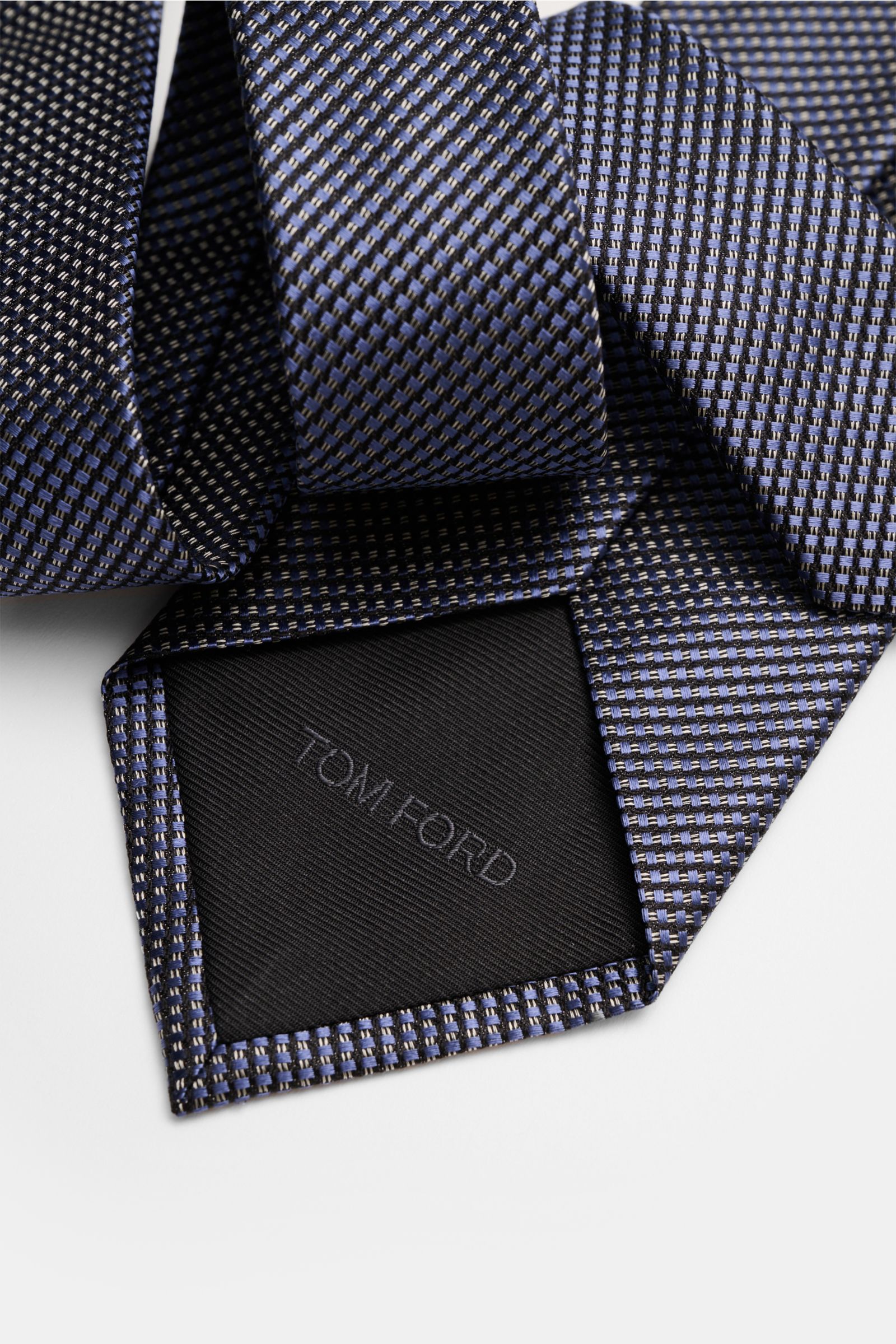 Close-up top view of the Tom Ford Seidenkrawatte rauchblau/schwarz/grau gemustert with a fine graphic weave and branded lining.

Description: Italienische Handwerkskunst: Dieser Krawatten-Klassiker von TOM FORD aus reiner Seide vereint zeitlose Eleganz