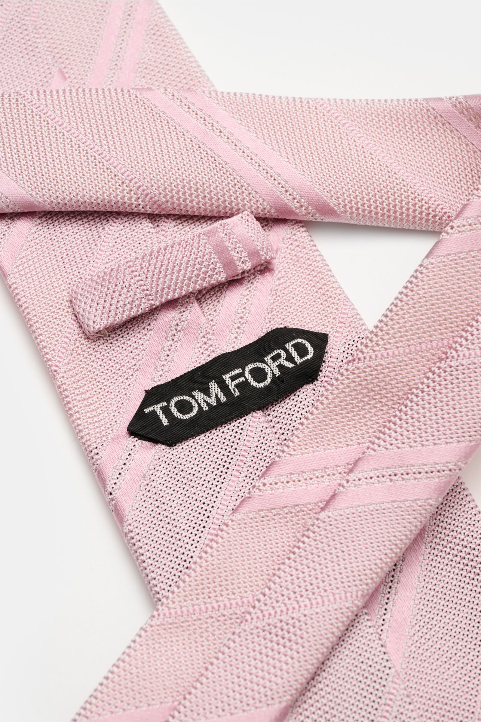 Close-up of the Tom Ford Seidenkrawatte altrosa/weiß gestreift showing its fine silk weave, subtle shine, and branded lining from a top-down perspective.

Description: Italienische Handwerkskunst: Dieser Krawatten-Klassiker von TOM FORD aus reiner Seid