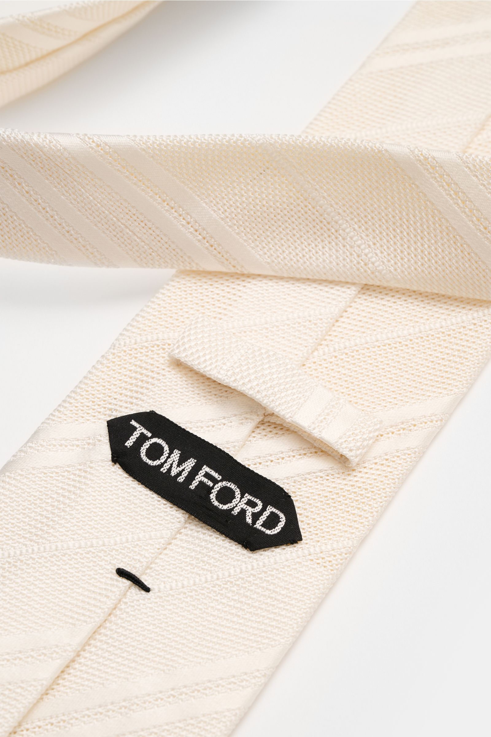 Close-up view of Tom Ford Seidenkrawatte creme/weiß gestreift showing its fine silk texture, subtle shine, and branded label.

Description: 
Italienische Handwerkskunst: Dieser Krawatten-Klassiker von TOM FORD aus reiner Seide vereint zeitlose Eleganz 