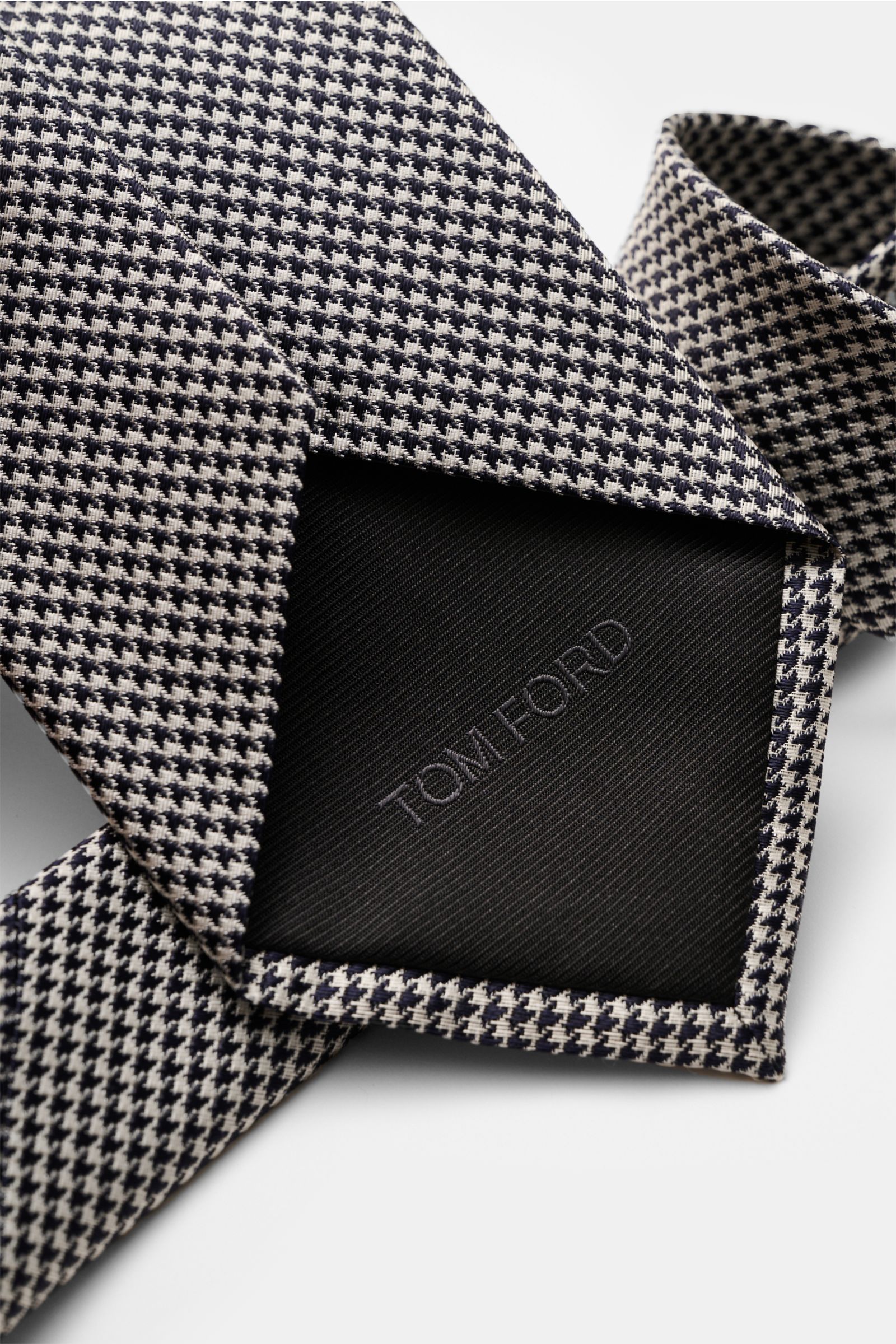 Tom Ford Seidenkrawatte dark navy/weiß gemustert, reine Seide, feines Webmuster, dezenter Glanz, gebrandeter Futterstoff, Made in Italy, 8 cm breit, Nahaufnahme von der Rückseite.