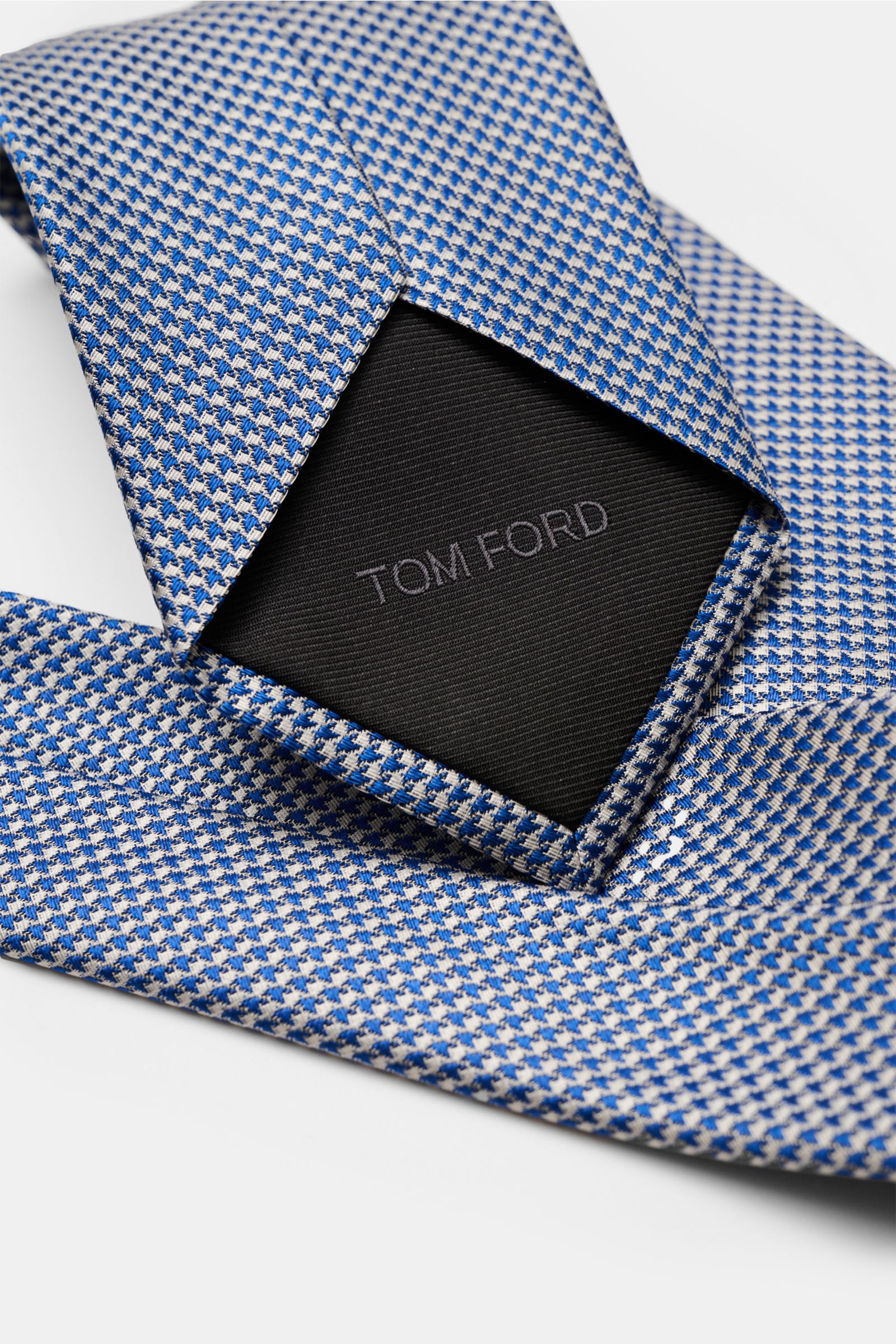 Tom Ford Seidenkrawatte blau/weiß gemustert, feines Webmuster, reine Seide, Blick von schräg oben, Markenlogo innen sichtbar.