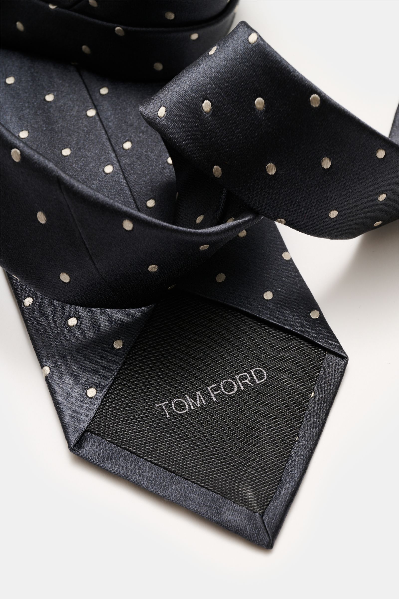 Tom Ford Seidenkrawatte anthrazit/creme gepunktet, aus reiner Seide mit dezentem Glanz, Logo-Stitching, monochromem Futter, 8 cm breit, made in Italy, Nahaufnahme von oben.