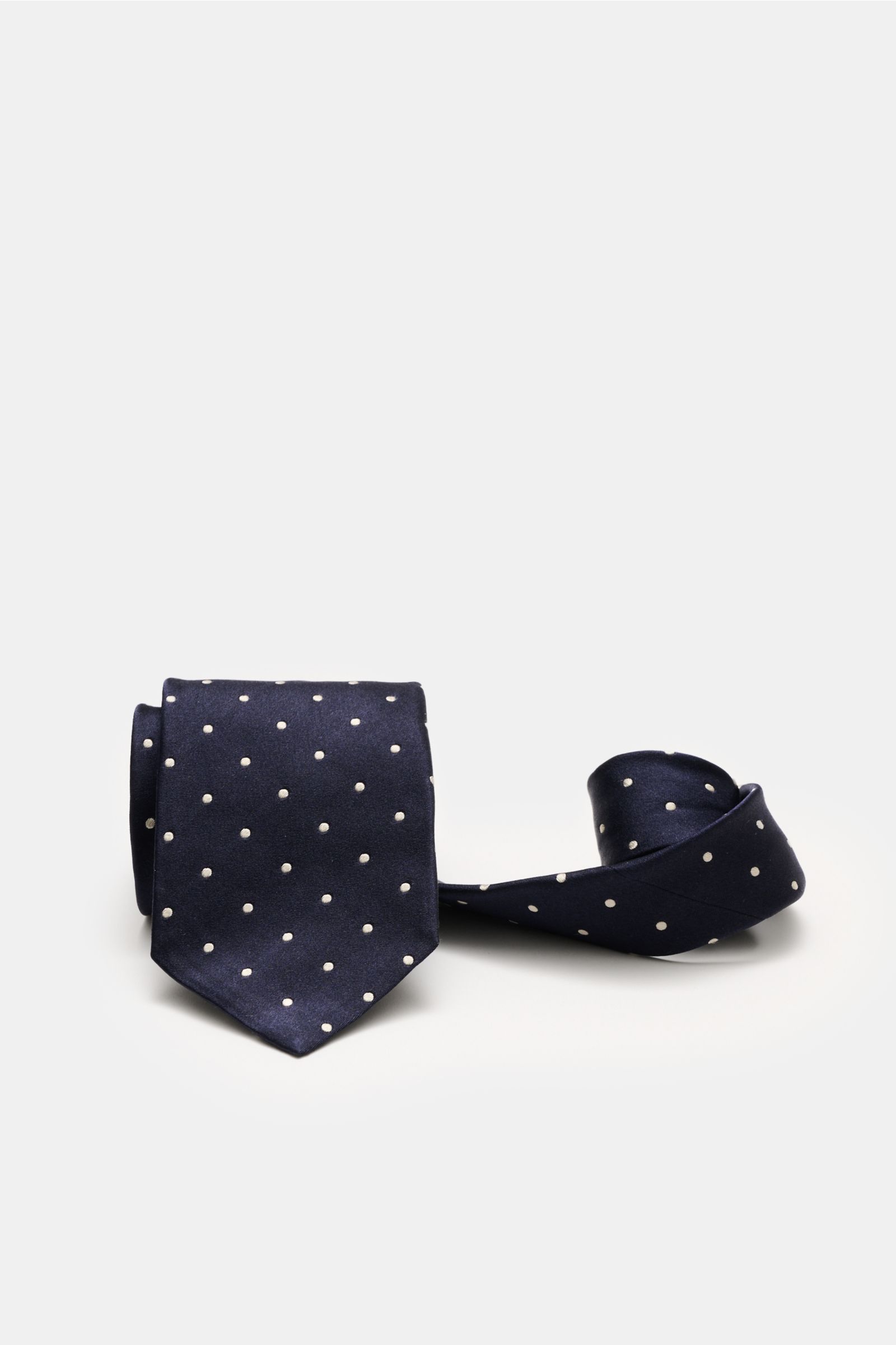 Front view of Tom Ford Seidenkrawatte navy/creme gepunktet, a navy silk tie with cream polka dots, rolled and folded.

Zeitloser Stil mit luxuriöser Note: Die Seidenkrawatte von TOM FORD überzeugt als elegantes Essential für formelle Anlässe und Office