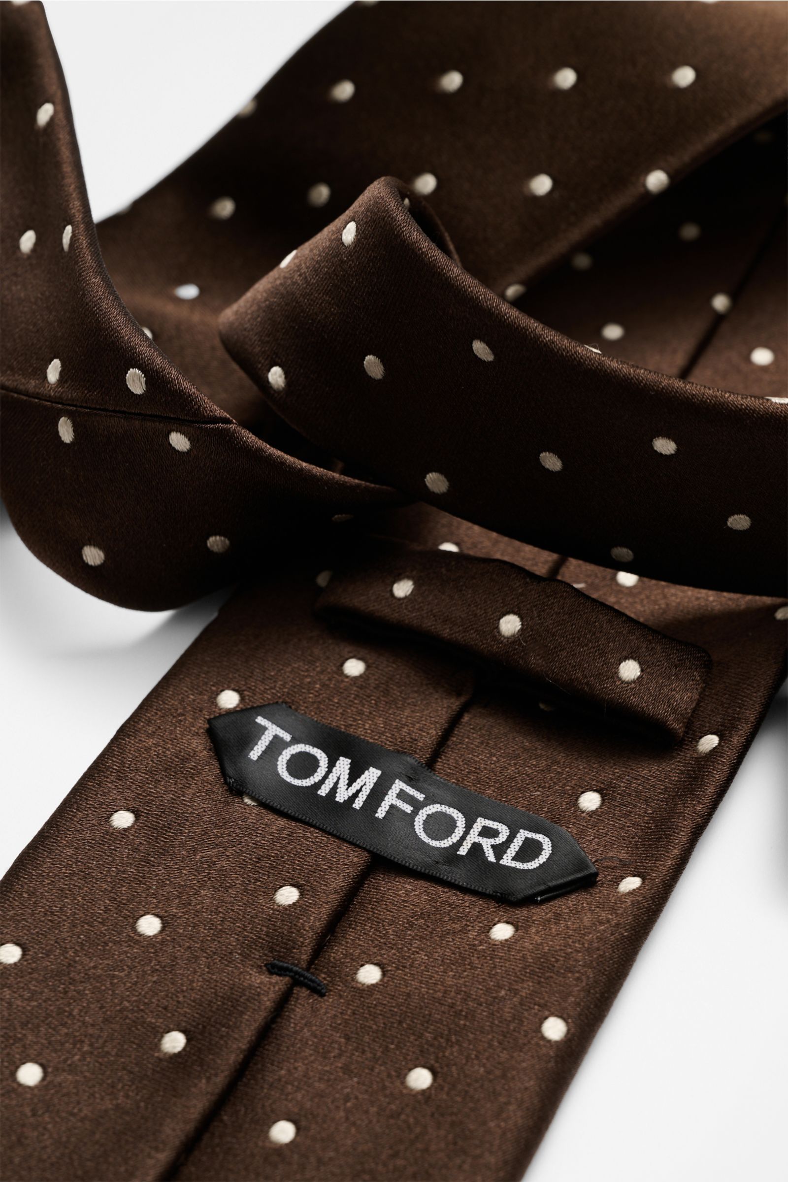 Close-up view of the Tom Ford Seidenkrawatte dunkelbraun/creme gepunktet silk tie with white polka dots and logo stitching, photographed from above.

Zeitloser Stil mit luxuriöser Note: Die Seidenkrawatte von TOM FORD überzeugt als elegantes Essential 