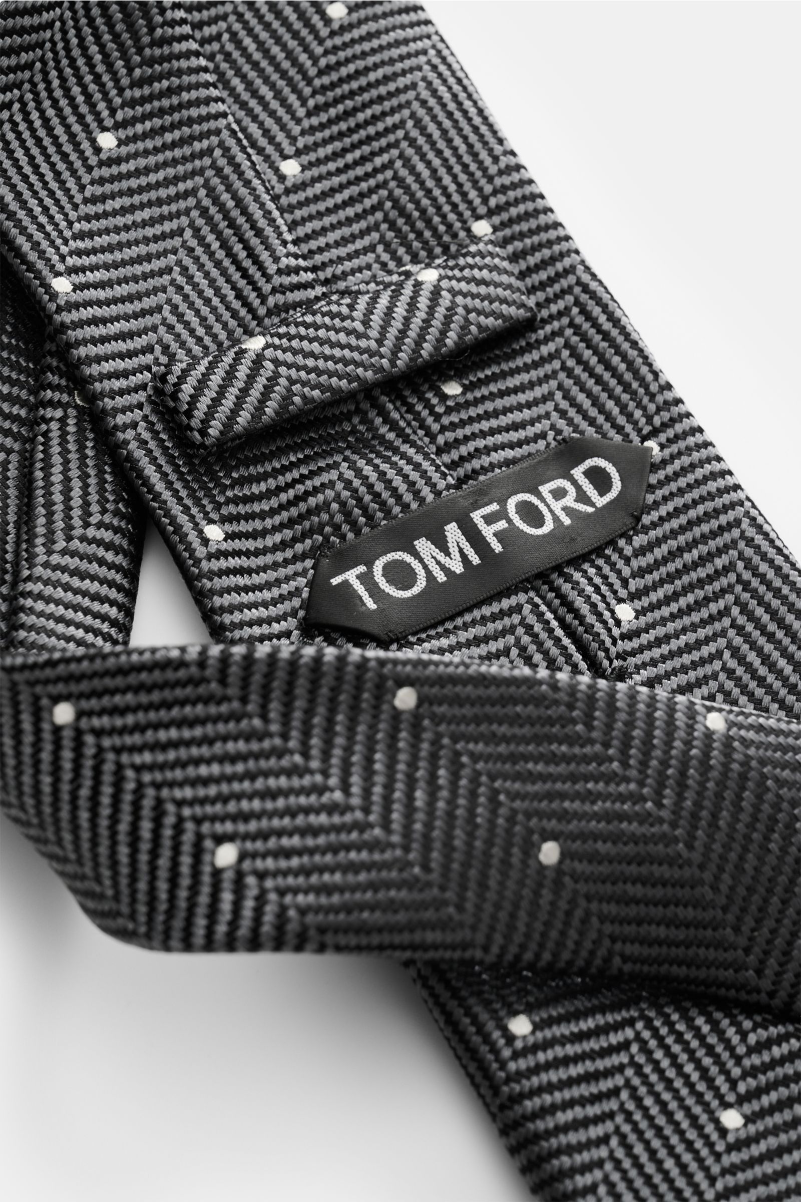 Tom Ford Seidenkrawatte dunkelgrau/schwarz/creme gemustert, Fischgratmuster mit Punkten, aus reiner Seide, Detailaufnahme von oben.